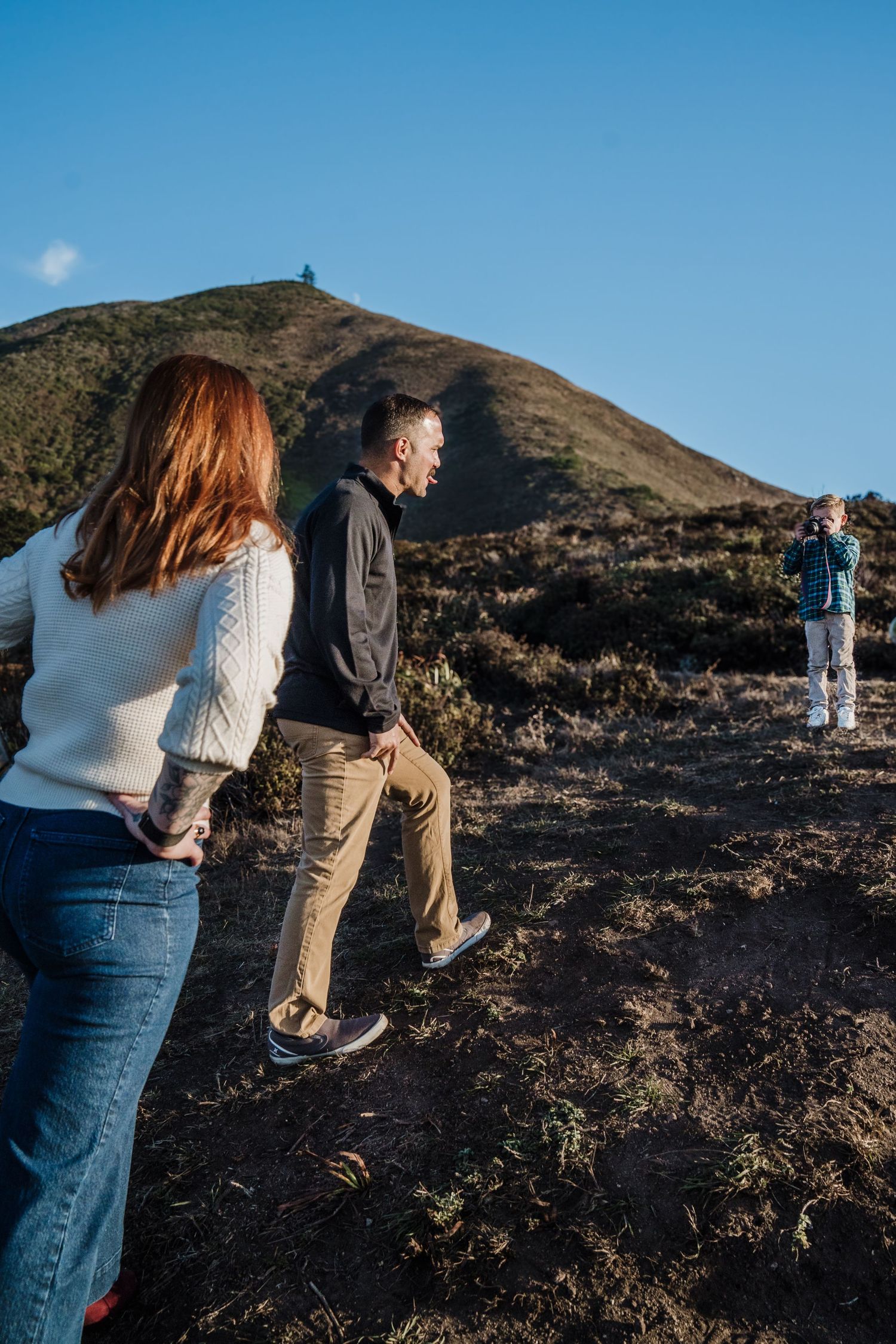 Two people walk up rocky volcanic terrain towards a hilltop observatory against blue sky and clouds.