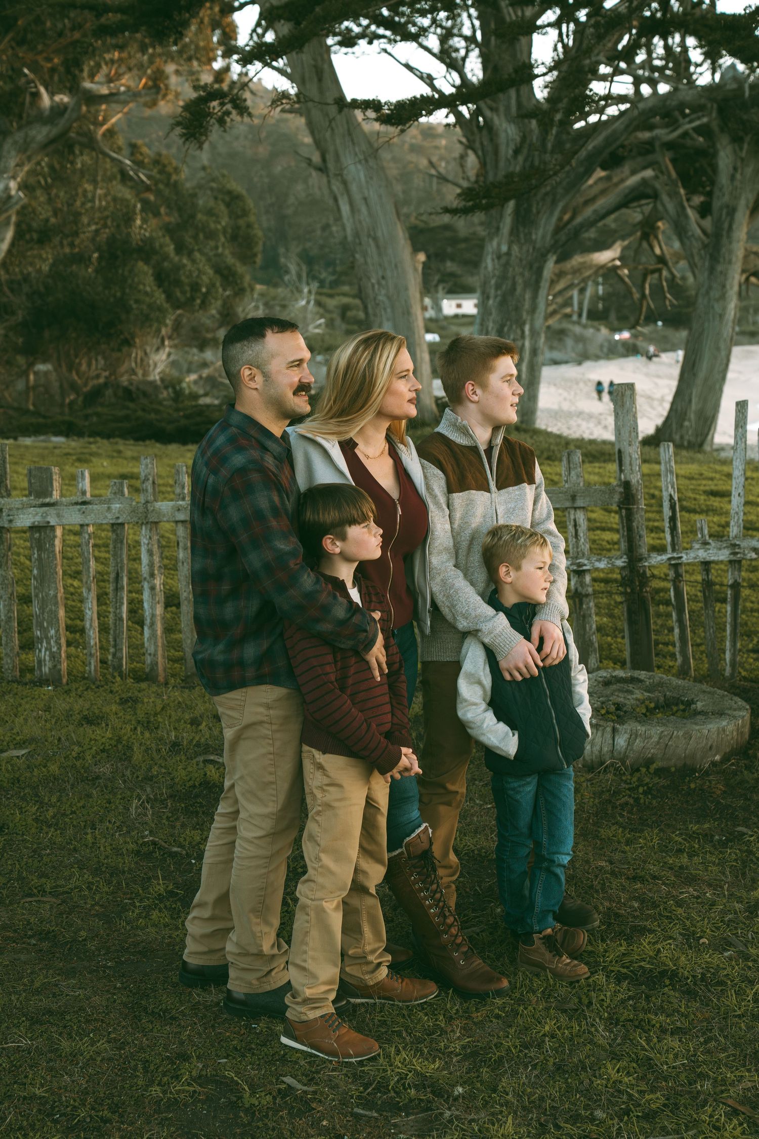Family enjoying a casual outdoor moment together in a rustic fenced area with trees.
