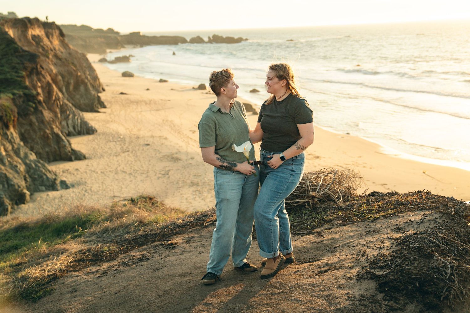 Two people enjoying a romantic sunset walk along a scenic beach with cliffs.