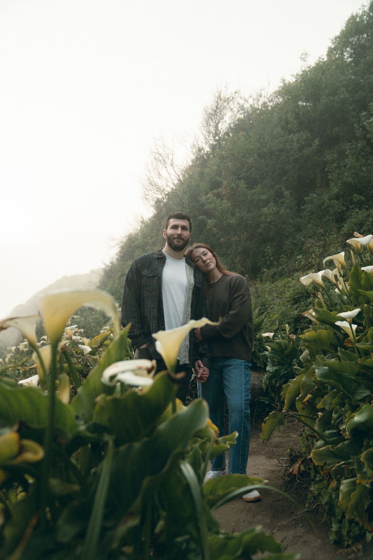 A couple posing surrounded by Cala Lilies on a foggy day in Big Sur.