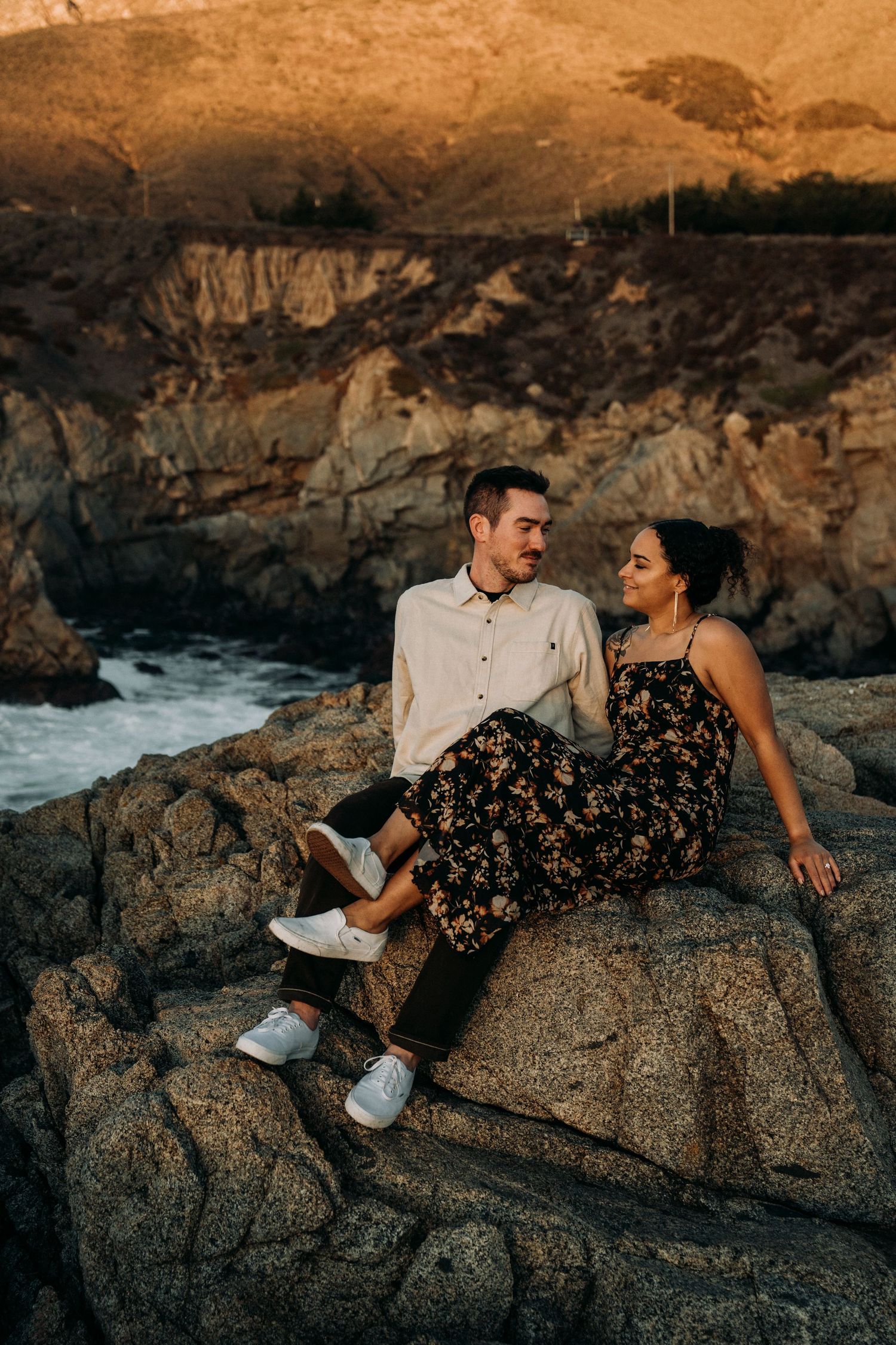 Couple sharing romantic moments on rocky coastal cliffs during golden hour.