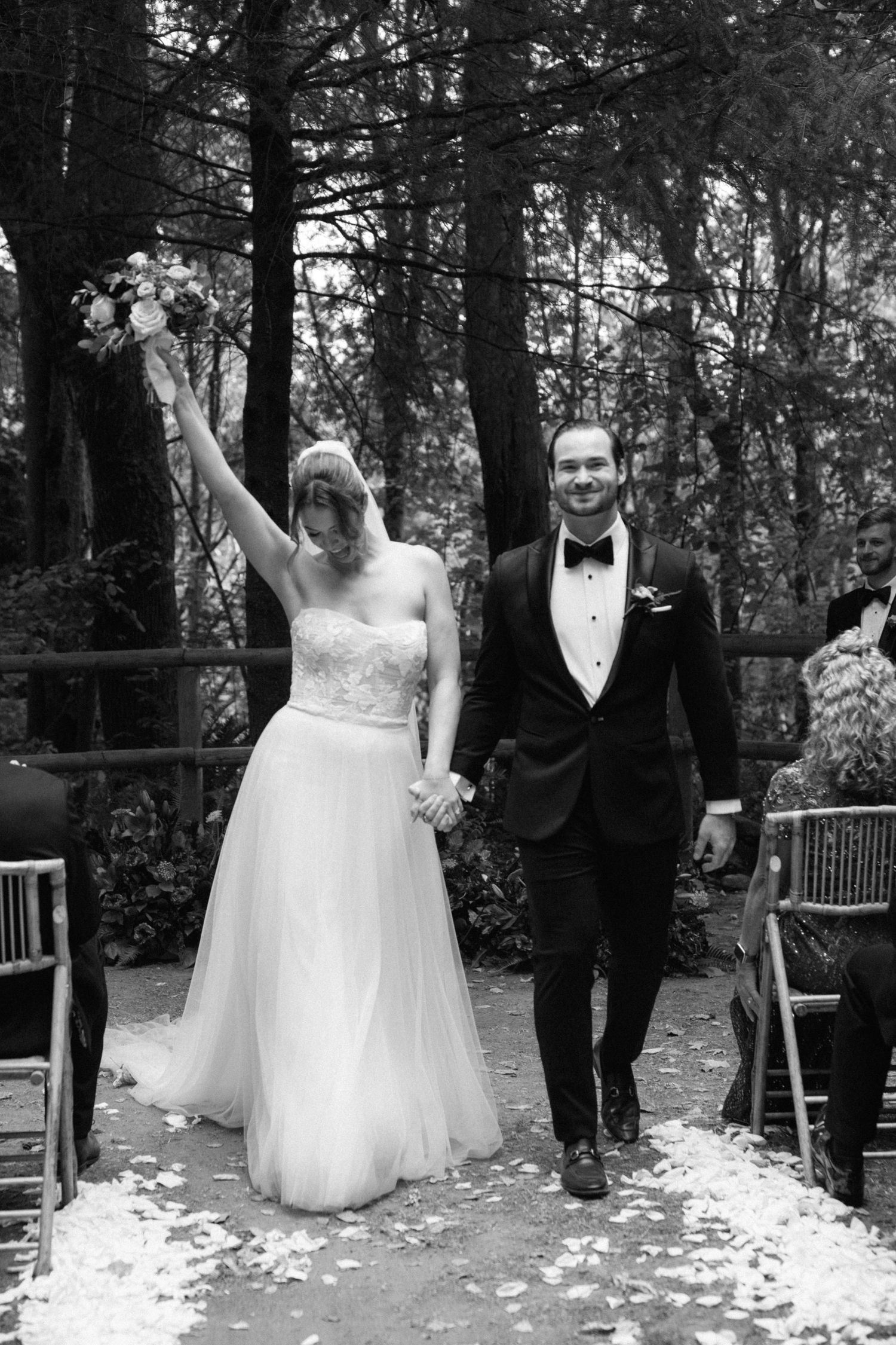 Black and white photos of newlyweds celebrating on forest path with flower petals.