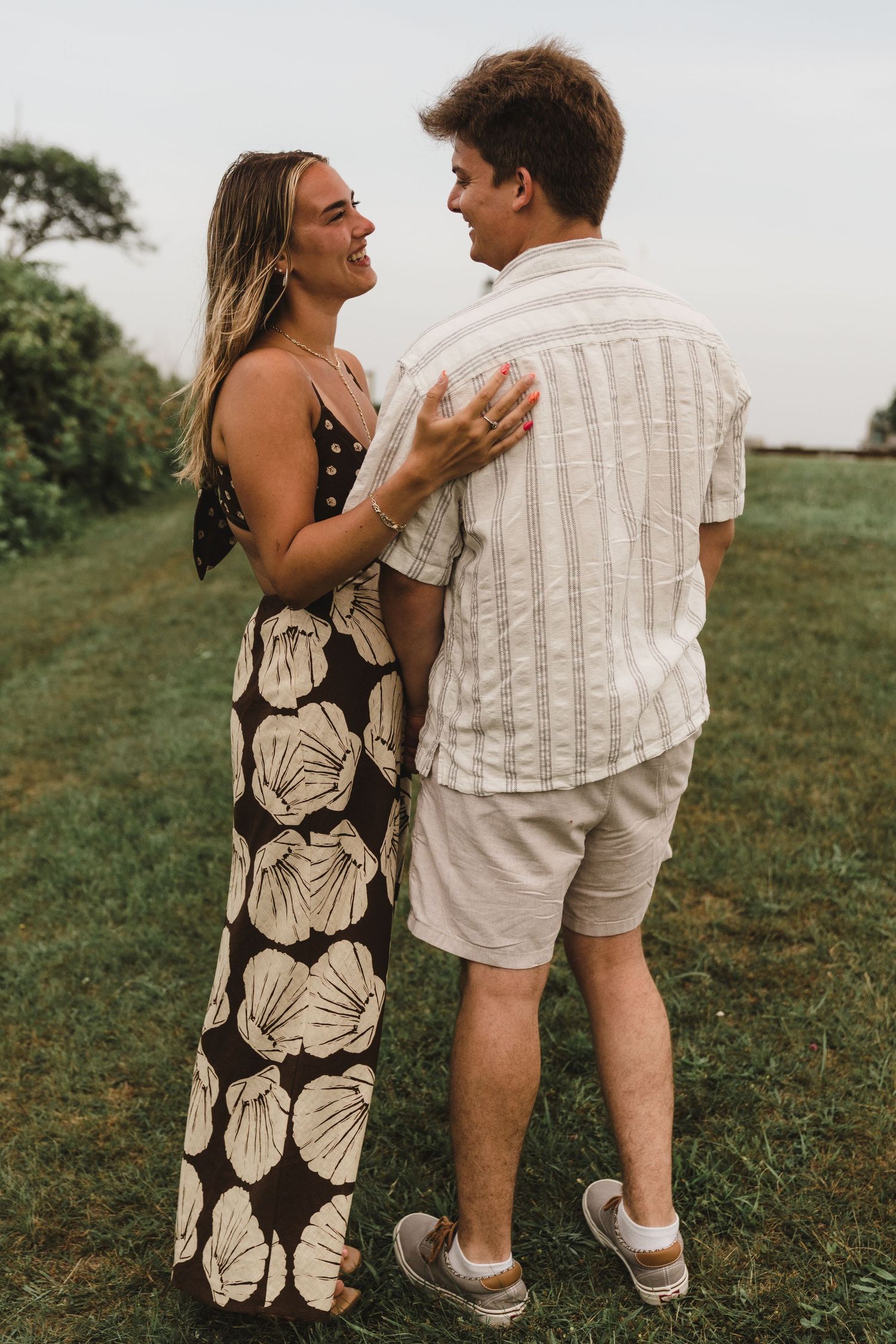 A couple shares a candid laughing moment outdoors while wearing coordinated summer outfits.