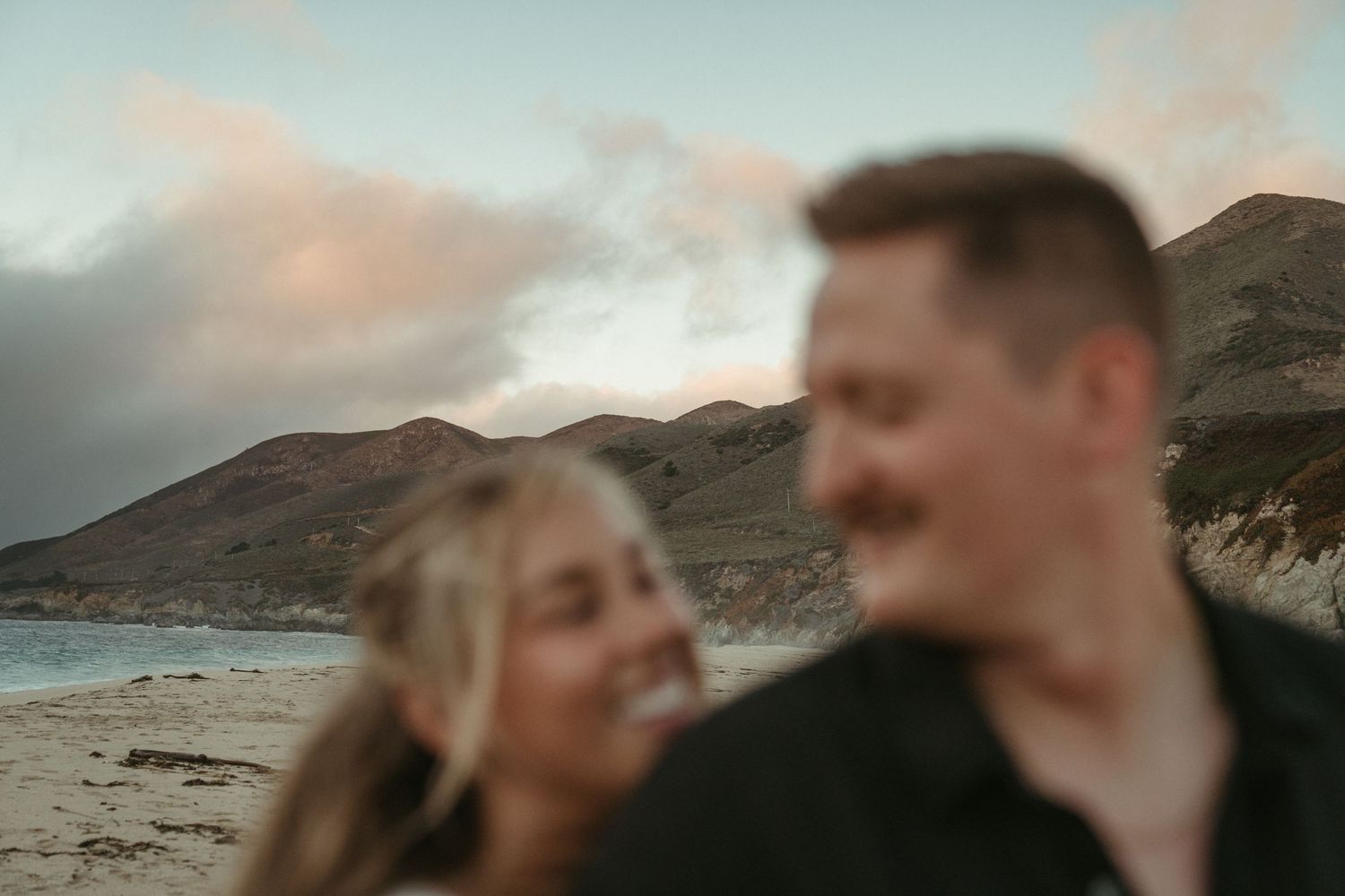 A romantic embrace against a dramatic coastal landscape with mountains in the background.