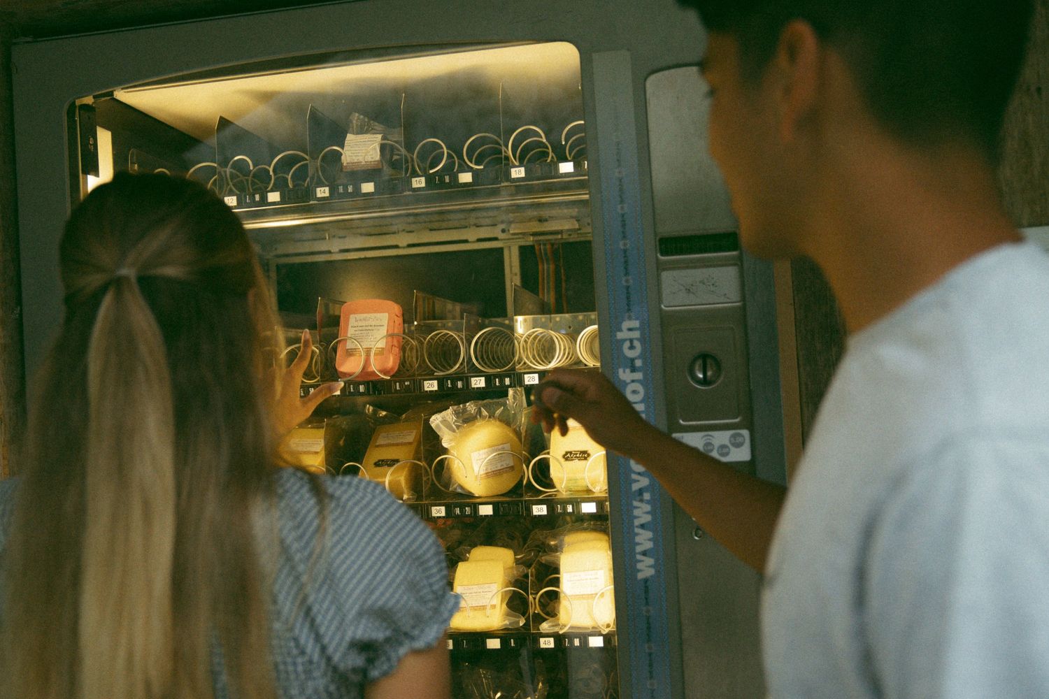Two people looking at drinks in a vending machine together.