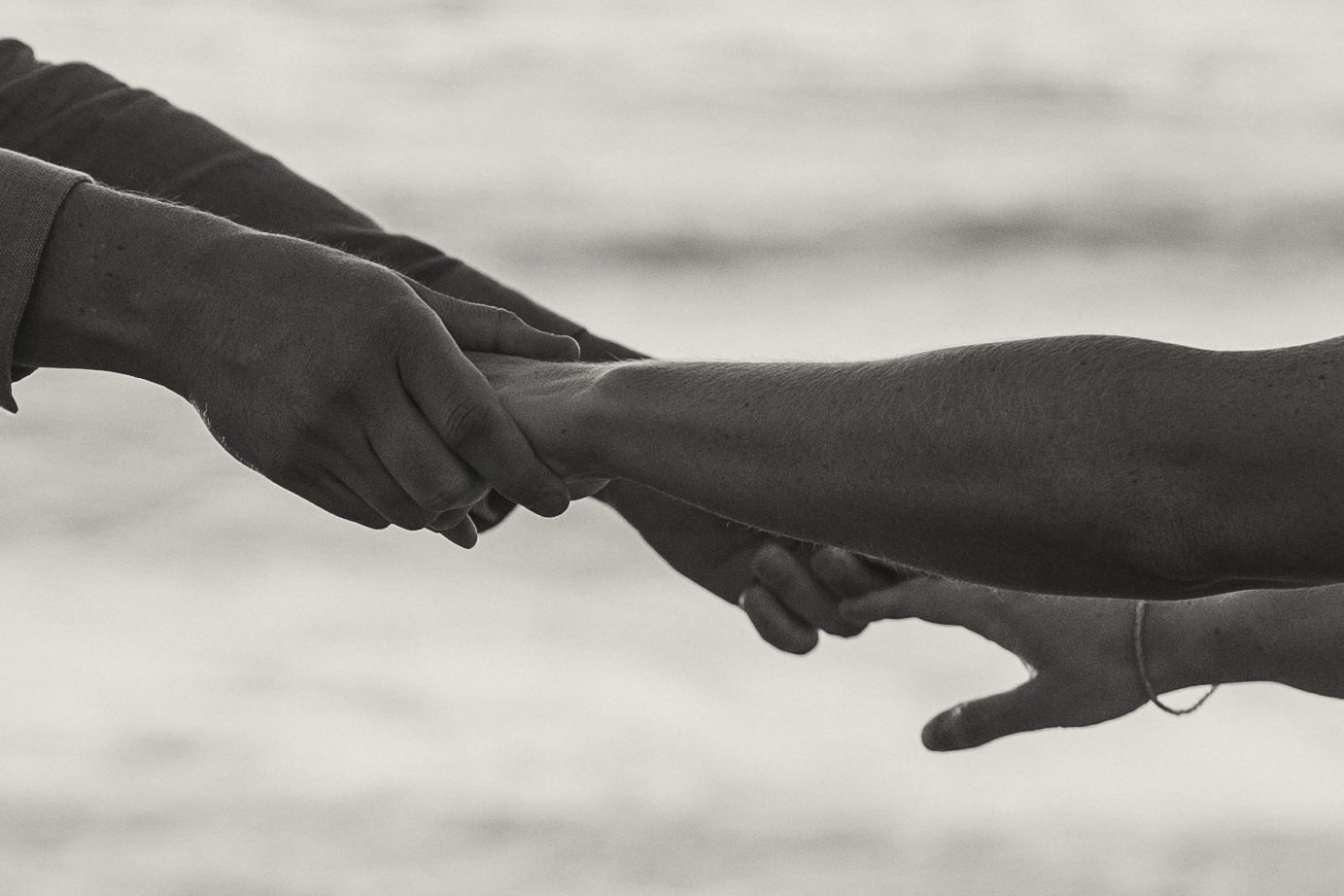 Two hands reaching towards each other against a minimalist gray background in black and white.