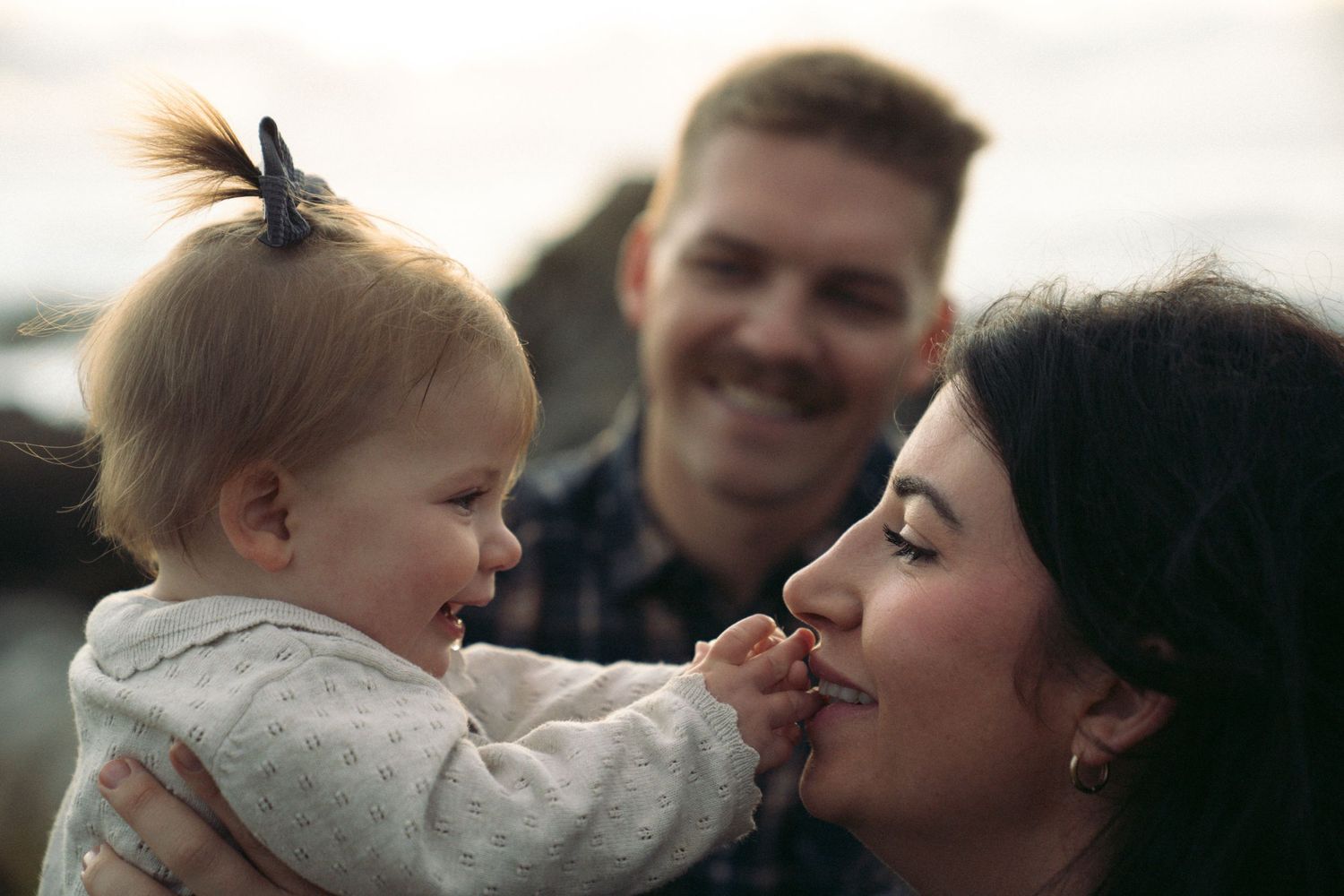 A tender family moment shows parents sharing affectionate interactions with their young child outdoors.
