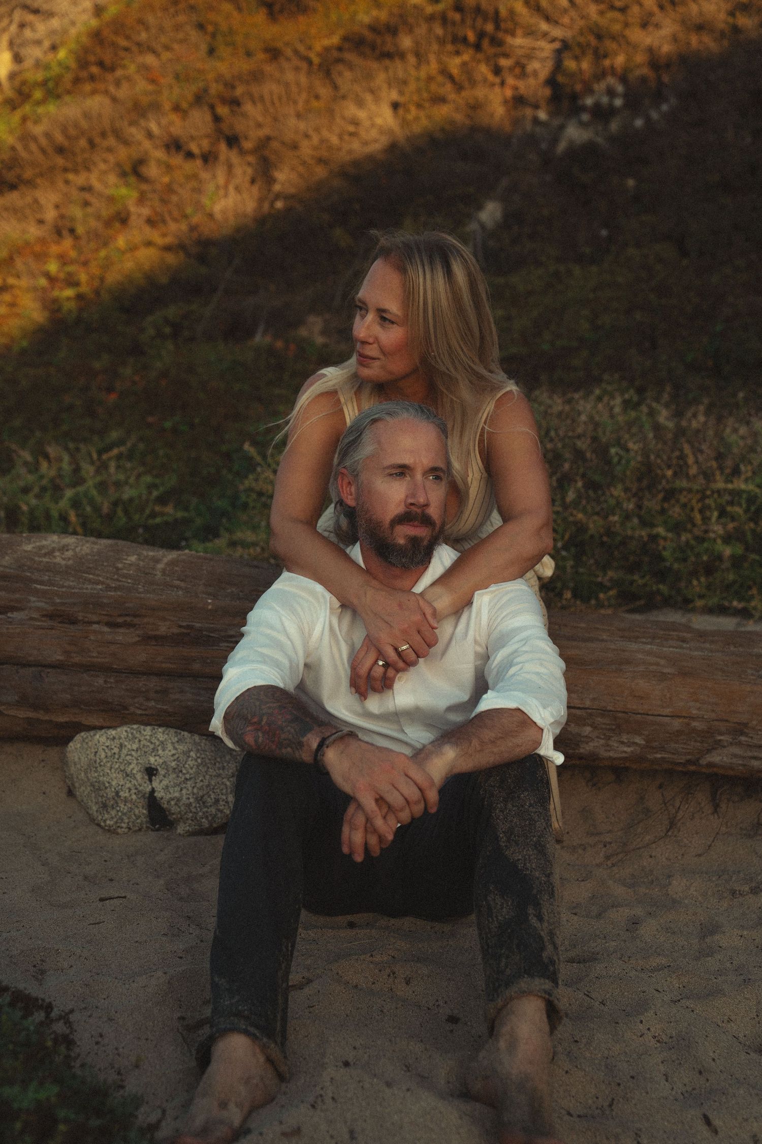 A couple shares an intimate moment sitting on a fallen log during golden hour in a natural outdoor setting.