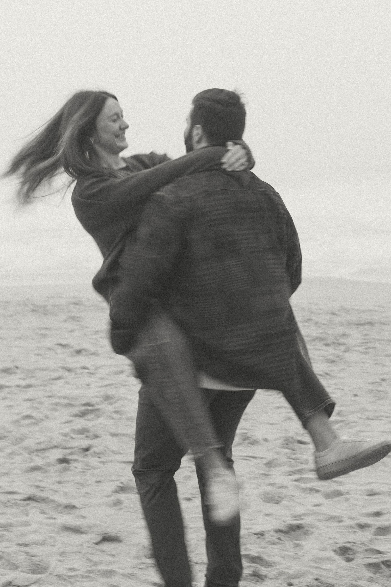 A black and white photo of a couple joyfully spinning on the Garrapata beach.