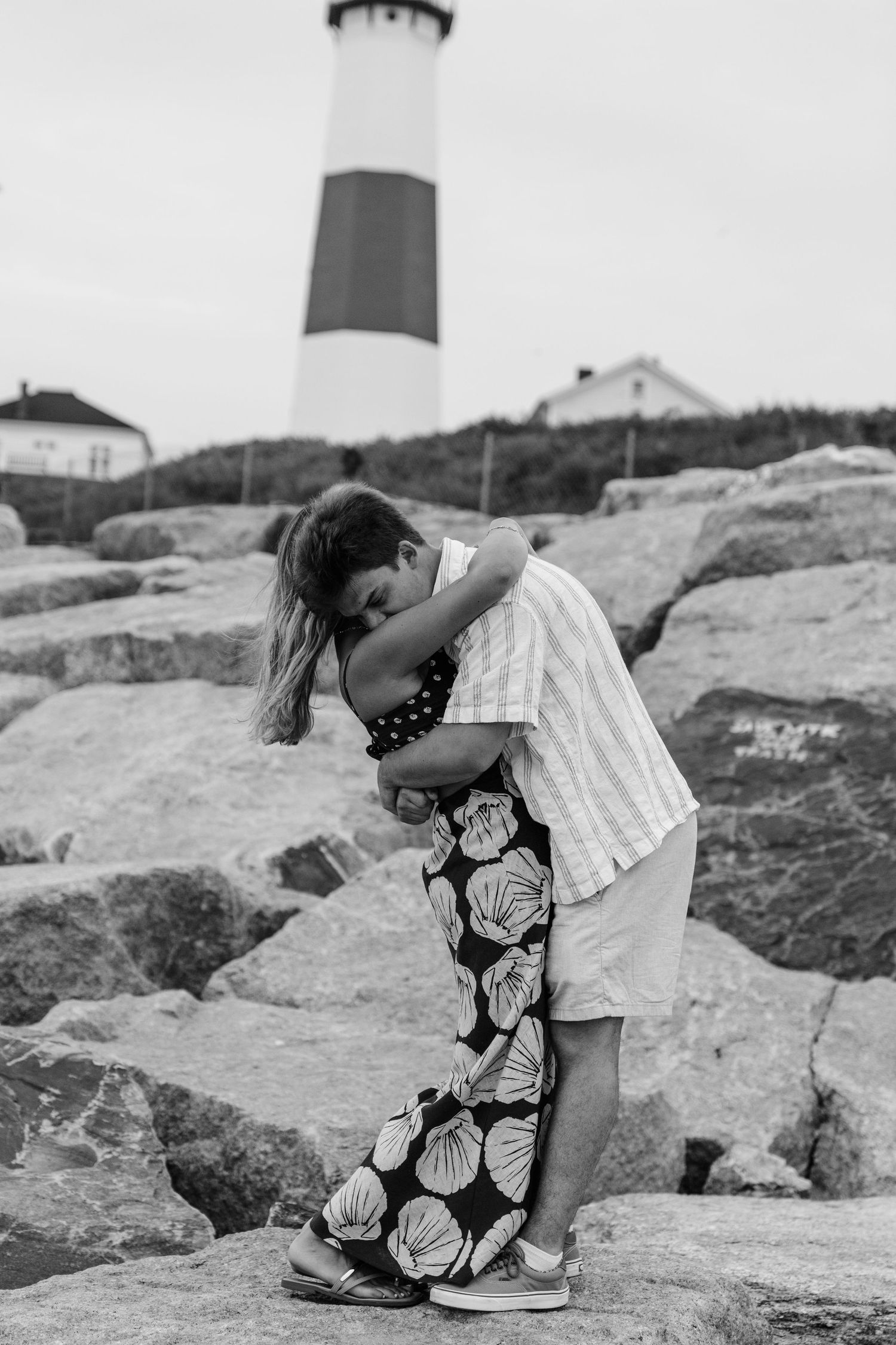 Black and white photo series of someone reading a map on coastal rocks near a lighthouse.
