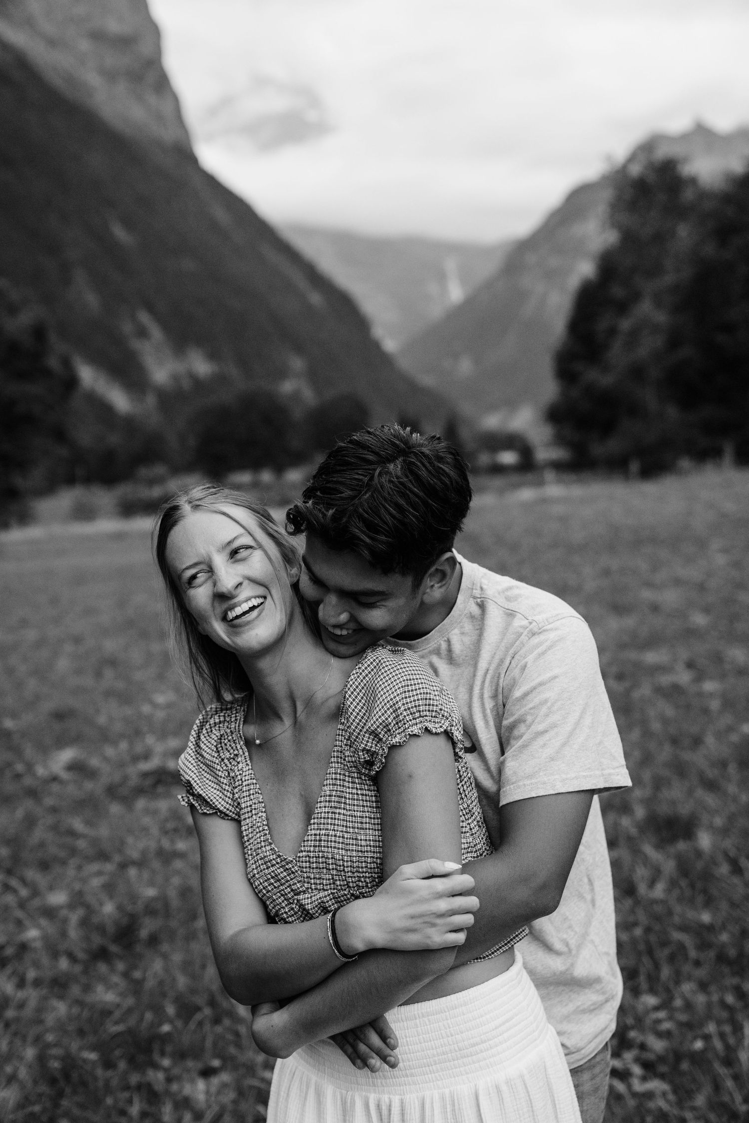 A couple shares a romantic moment together in a meadow with dramatic mountain peaks in the background.