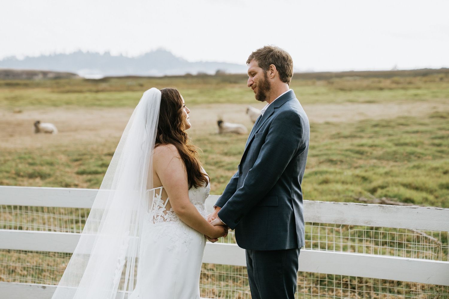 A couple in wedding attire stands together on a scenic mountain meadow during their outdoor ceremony.