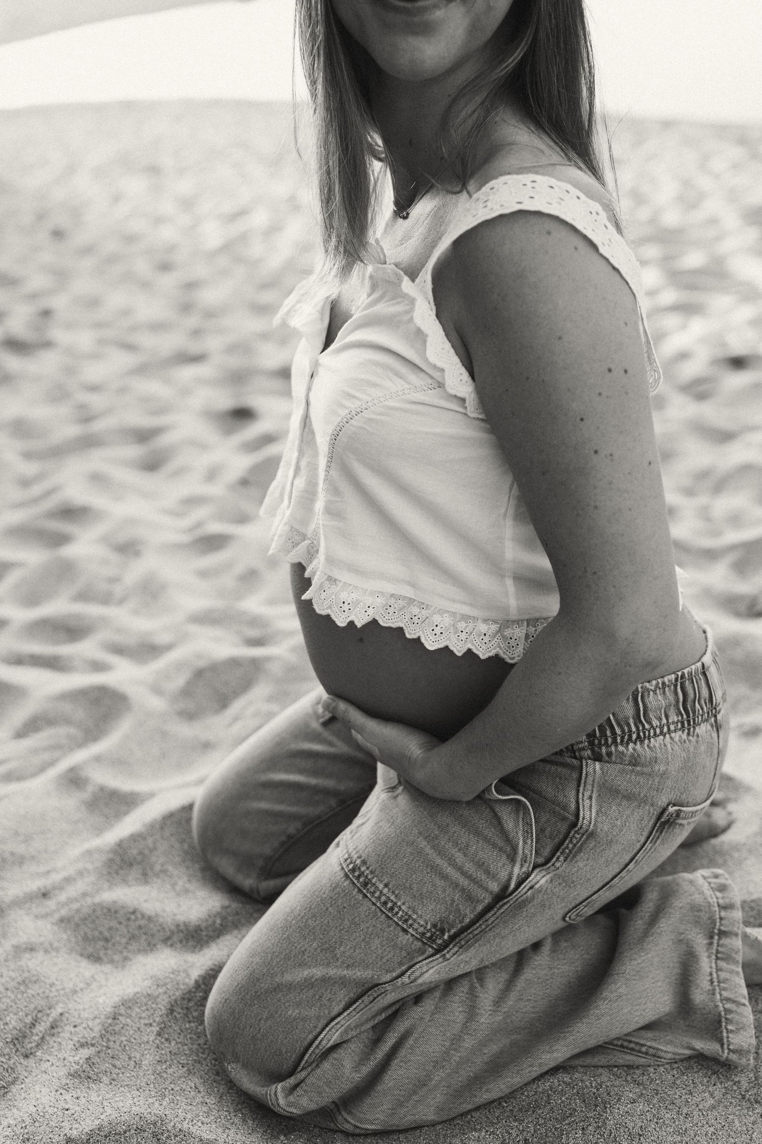 Person sitting in casual denim on sandy beach in black and white photography.