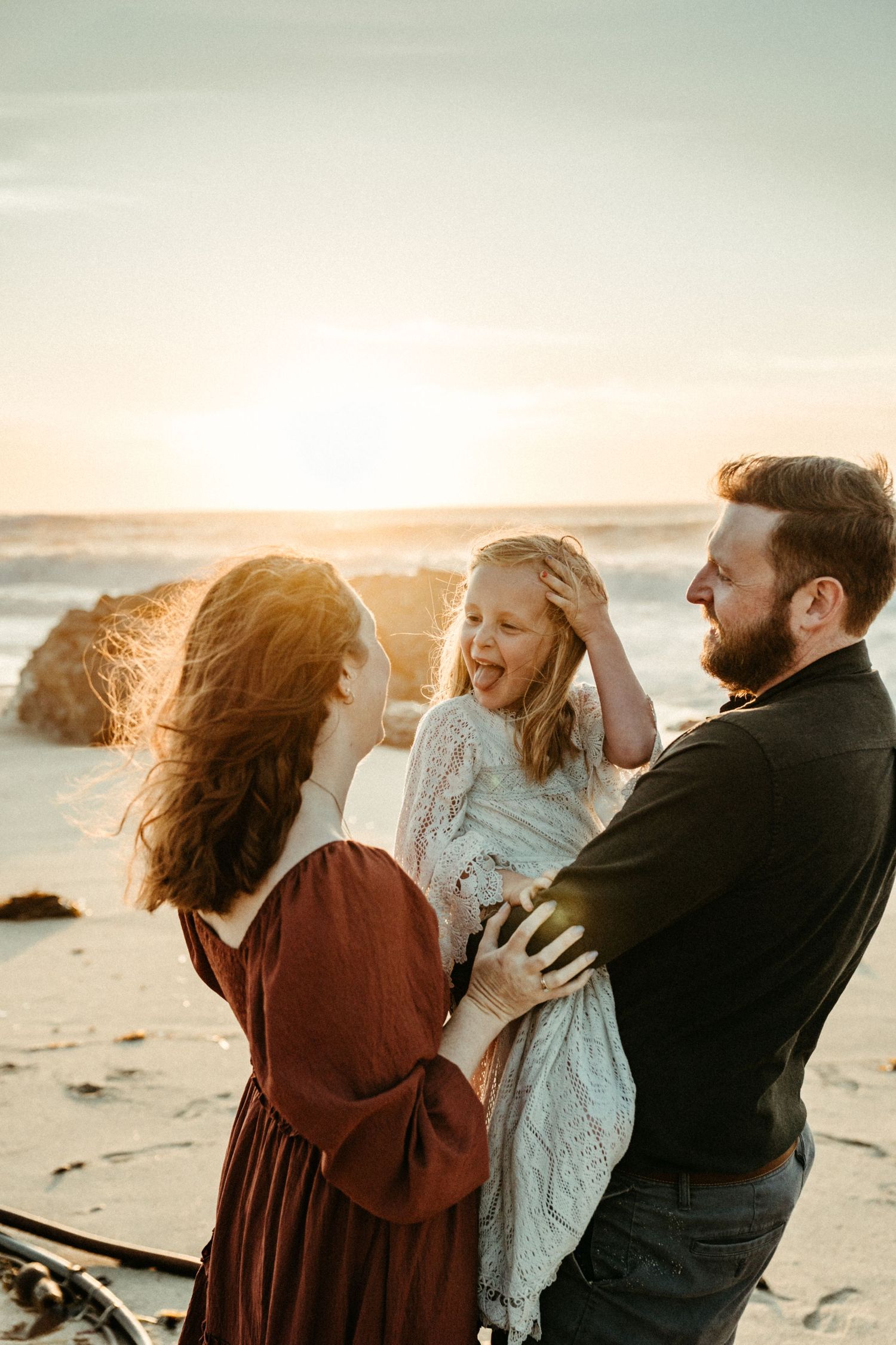 A family shares tender moments together on a sandy beach at sunset in a series of candid photographs.
