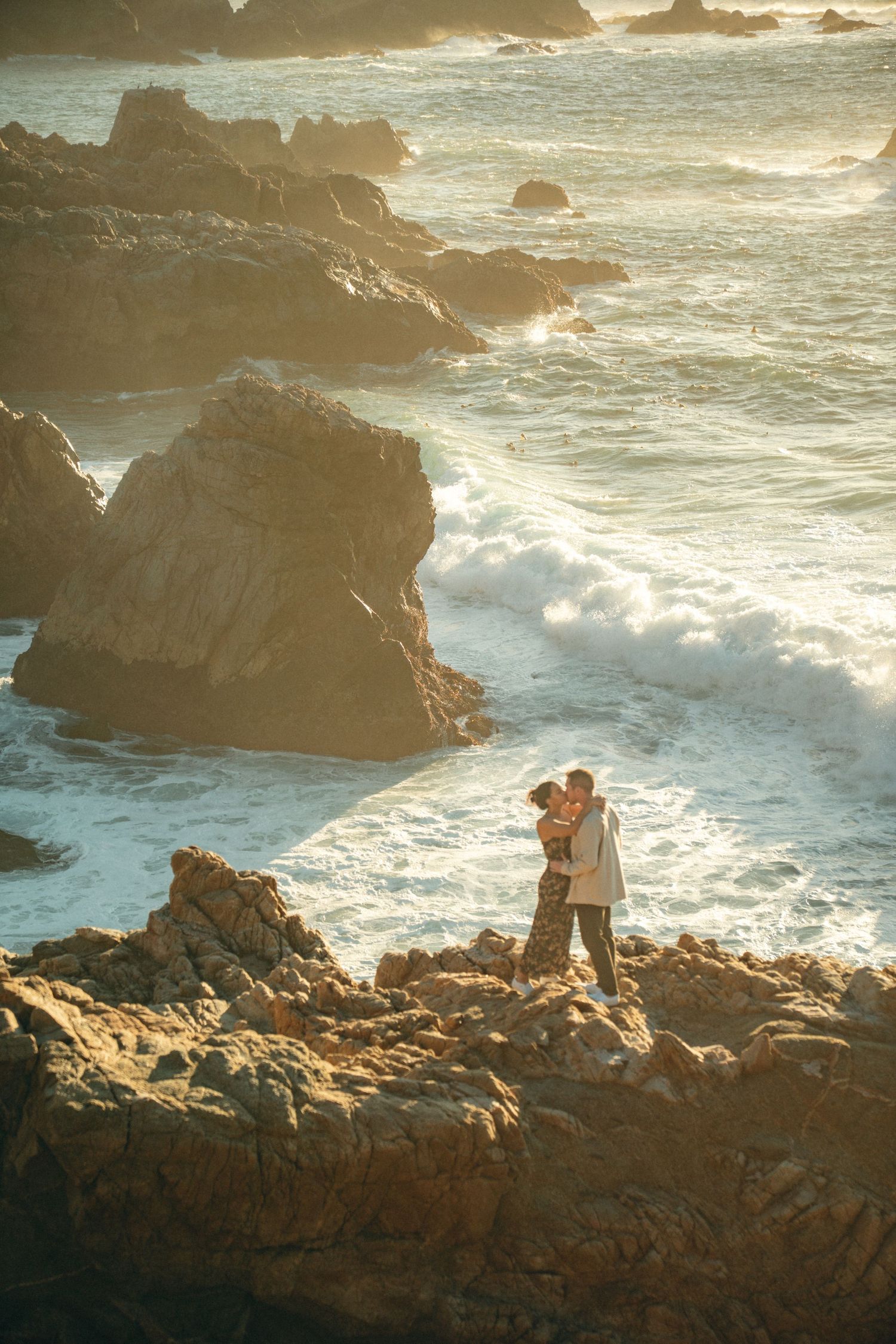 Dramatic coastal landscape with waves crashing against rocky cliffs during golden sunset hour.