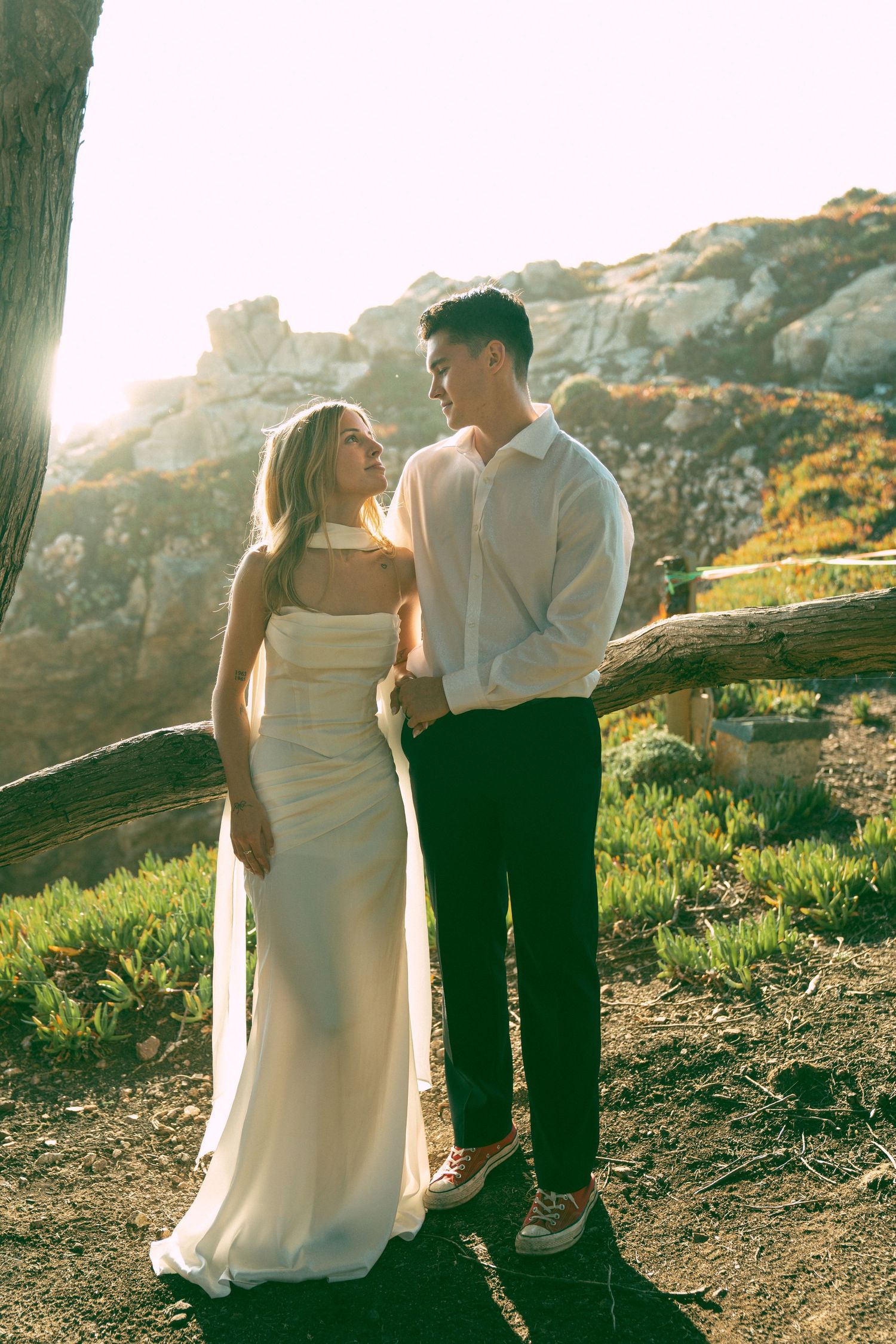 Romantic couple in wedding attire share intimate moments at sunset on a hillside overlooking scenic mountain views.