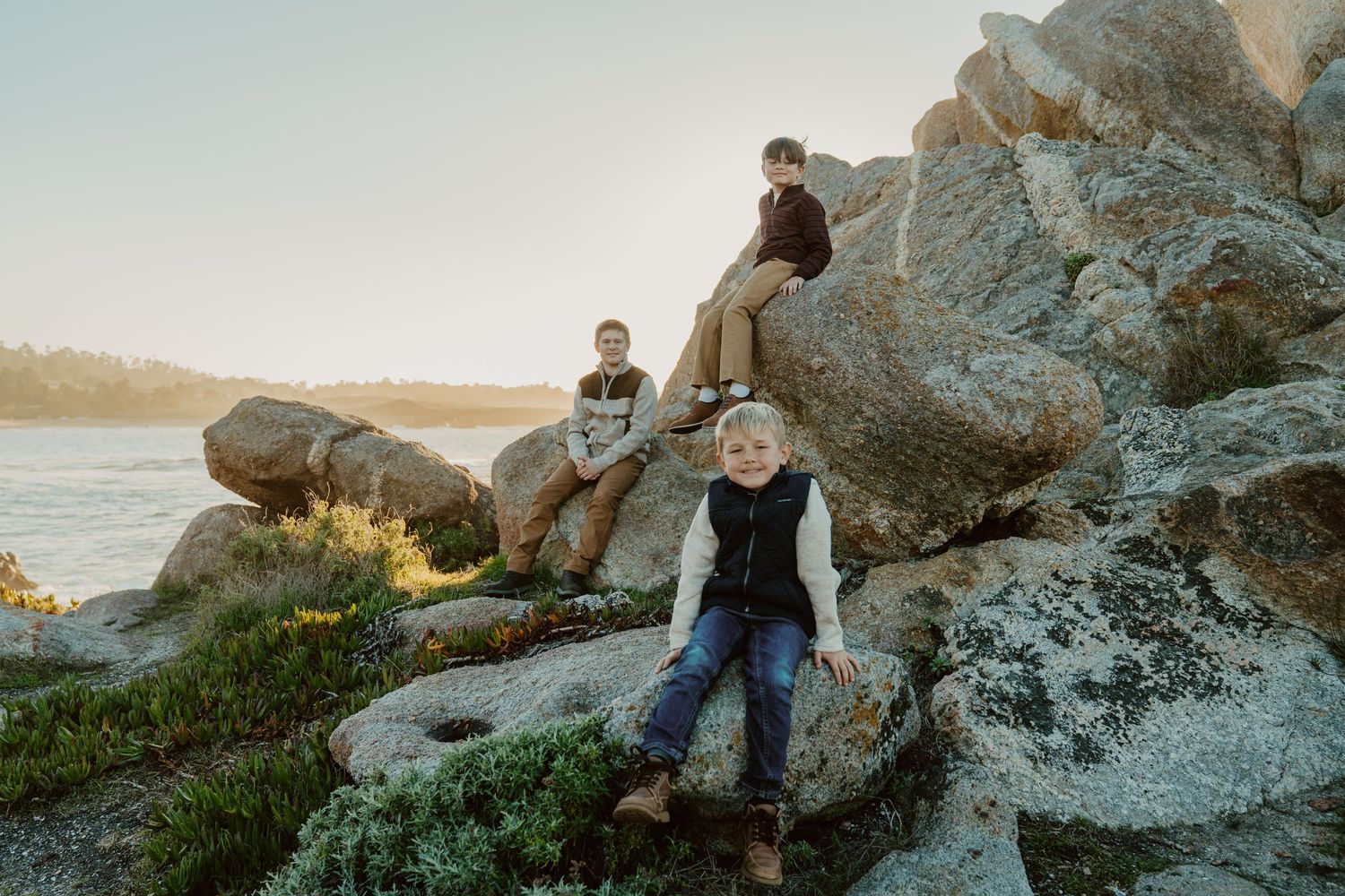 Family enjoying sunset together while exploring rocky coastal landscape at beach during golden hour.