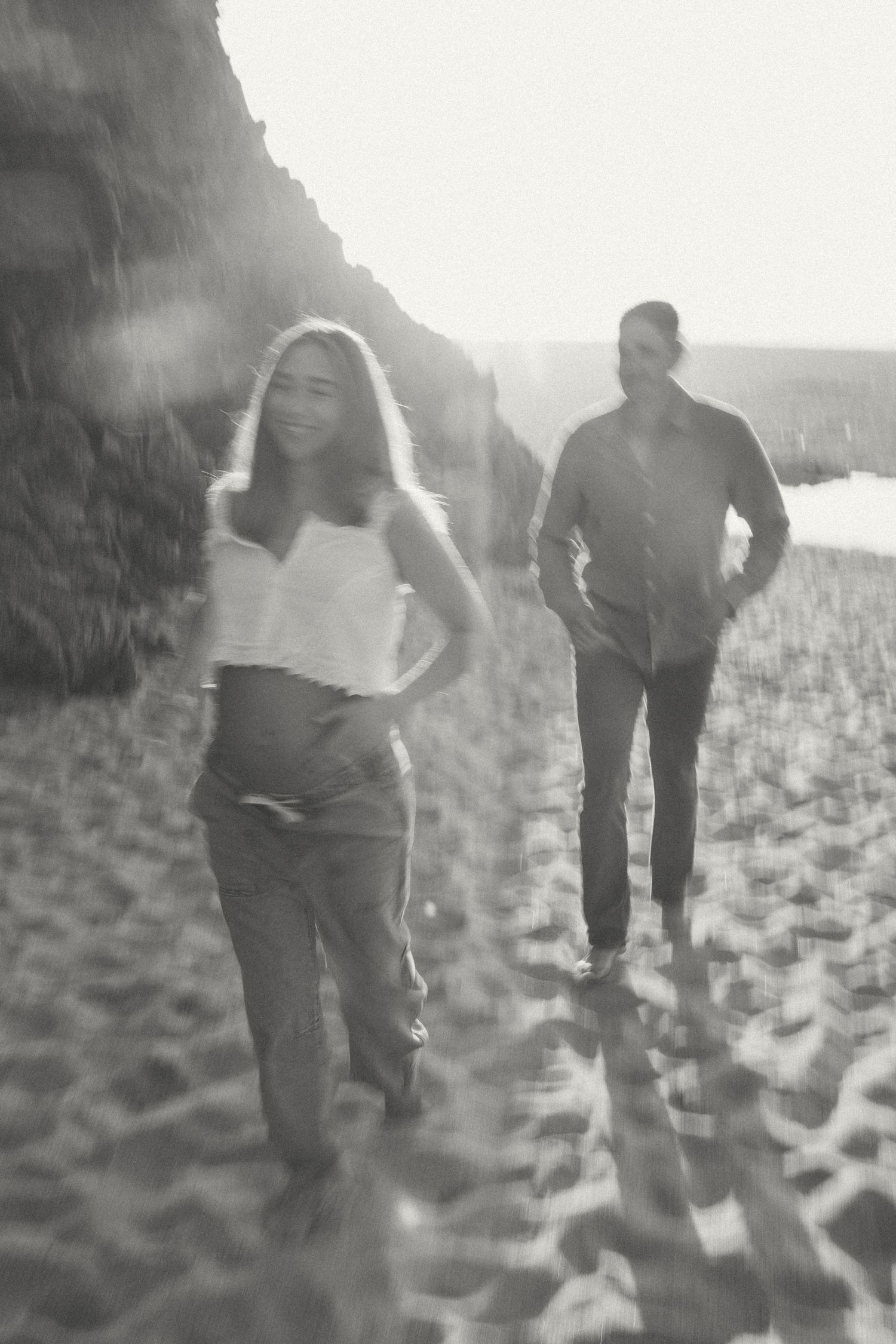 Multiple blurred black and white photos show people walking on a beach at sunset.