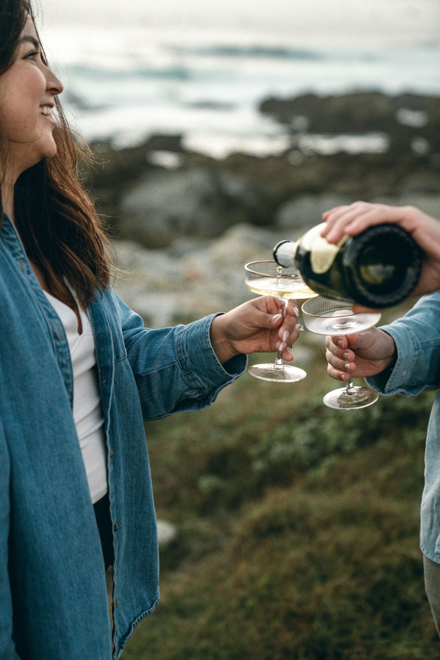 Two people toasting with champagne glasses against a coastal backdrop.