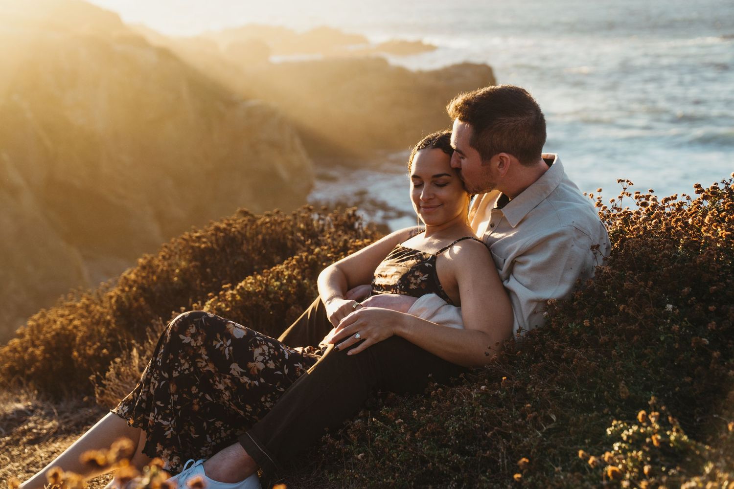 Intimate coastal photoshoot during golden hour with sunlit cliffs and ocean backdrop.