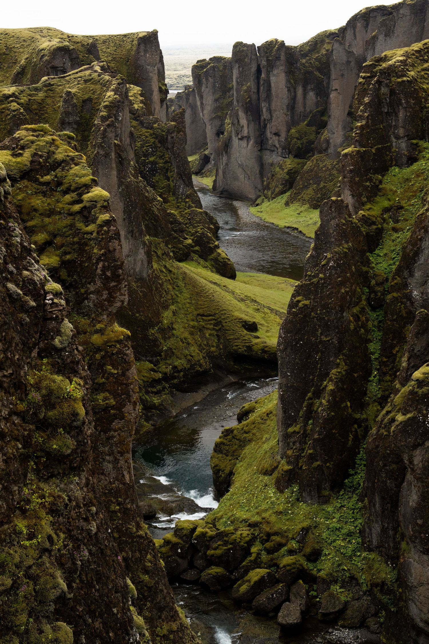A winding river flows through moss-covered canyon walls in Fjadrargljufur, Iceland, creating a dramatic landscape.