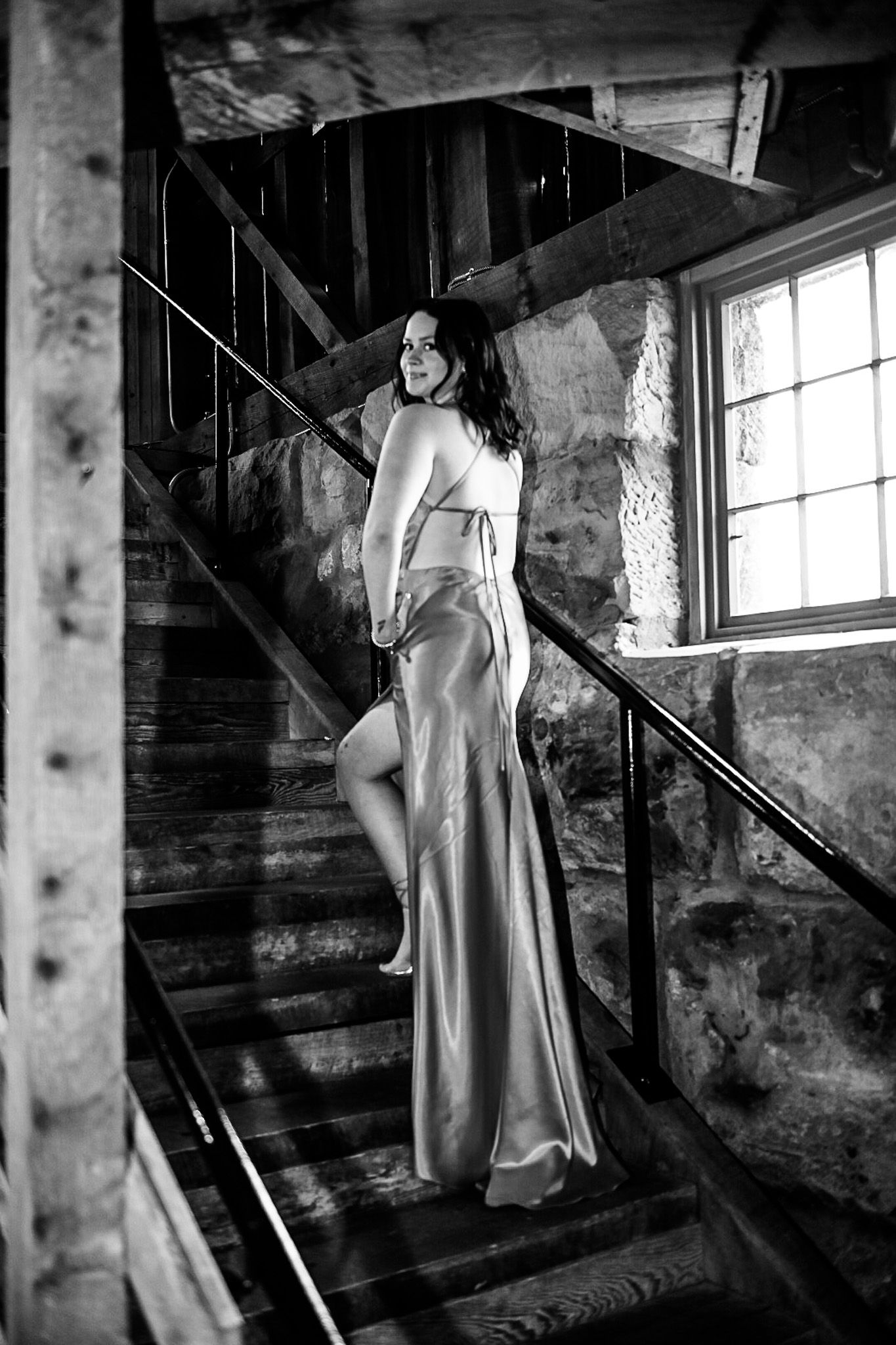 Teen poses for homecoming going up the stairs in a long pink dress looking over her shoulder. Image is in black and white