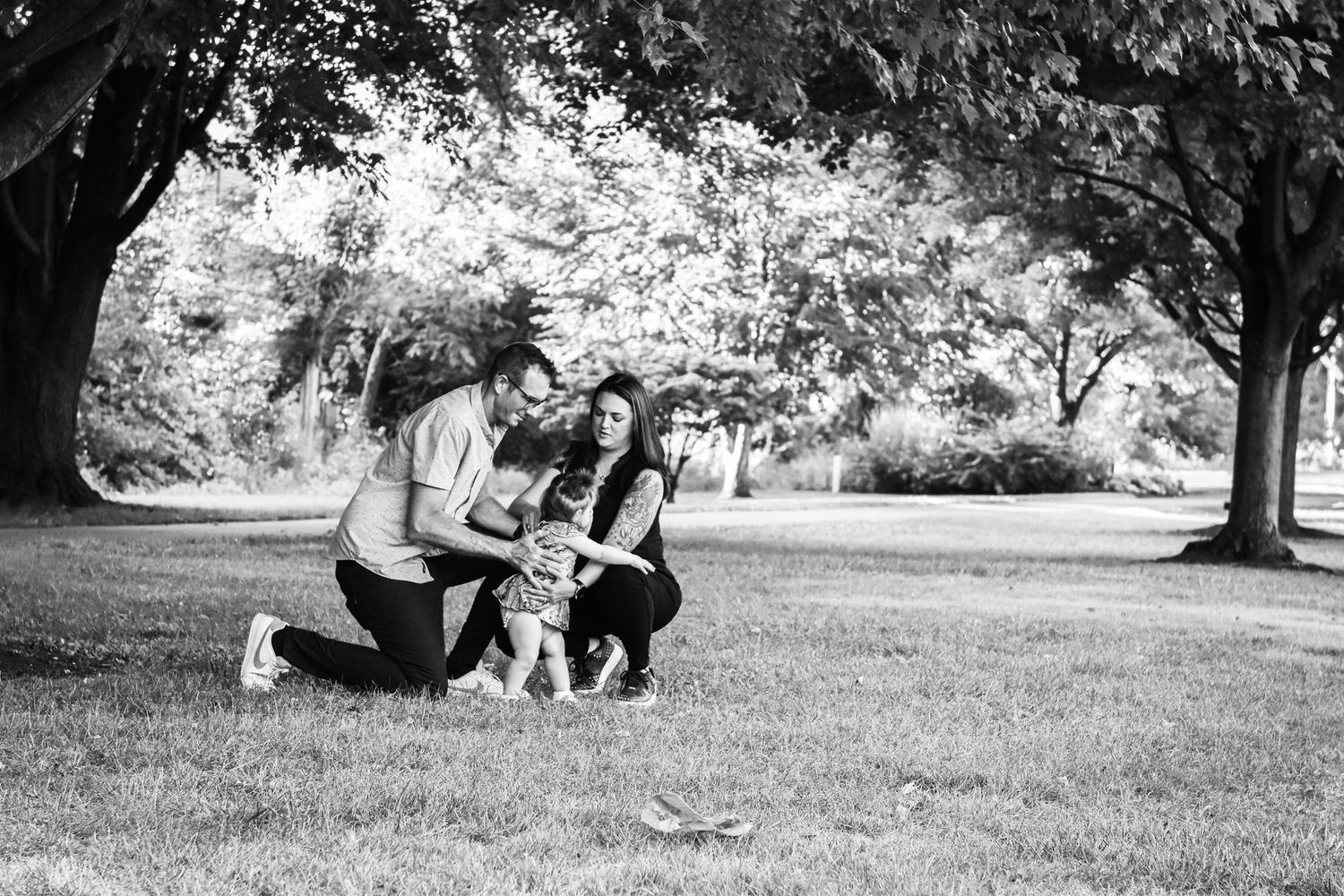 Candid image of family playing with toddler in park. Image is black and white