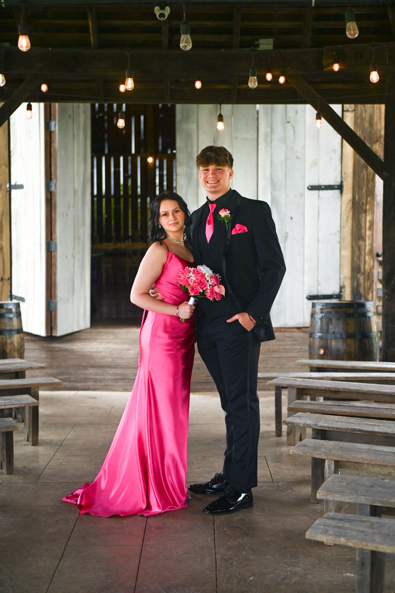 Dates for homecoming pose in front of a barn, under a gazebo with twinkling lights.