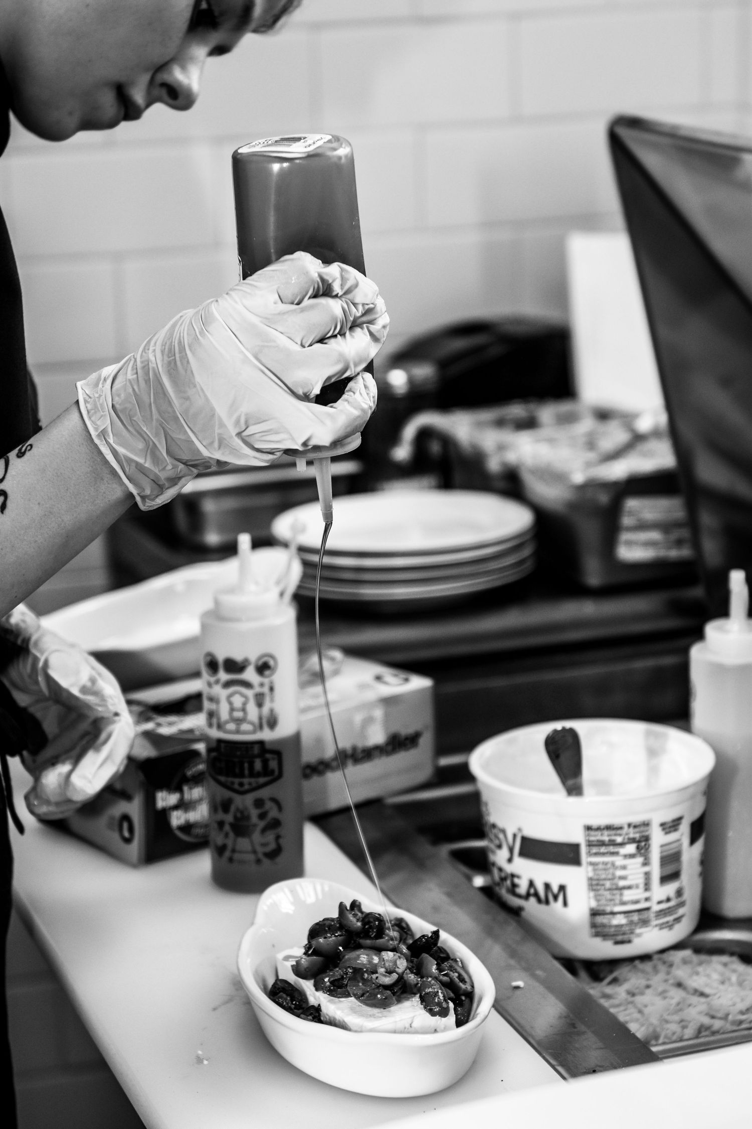 Interior photo of The Social at the Stone House, a chef adds the final touch to a dish. Image is in black and white