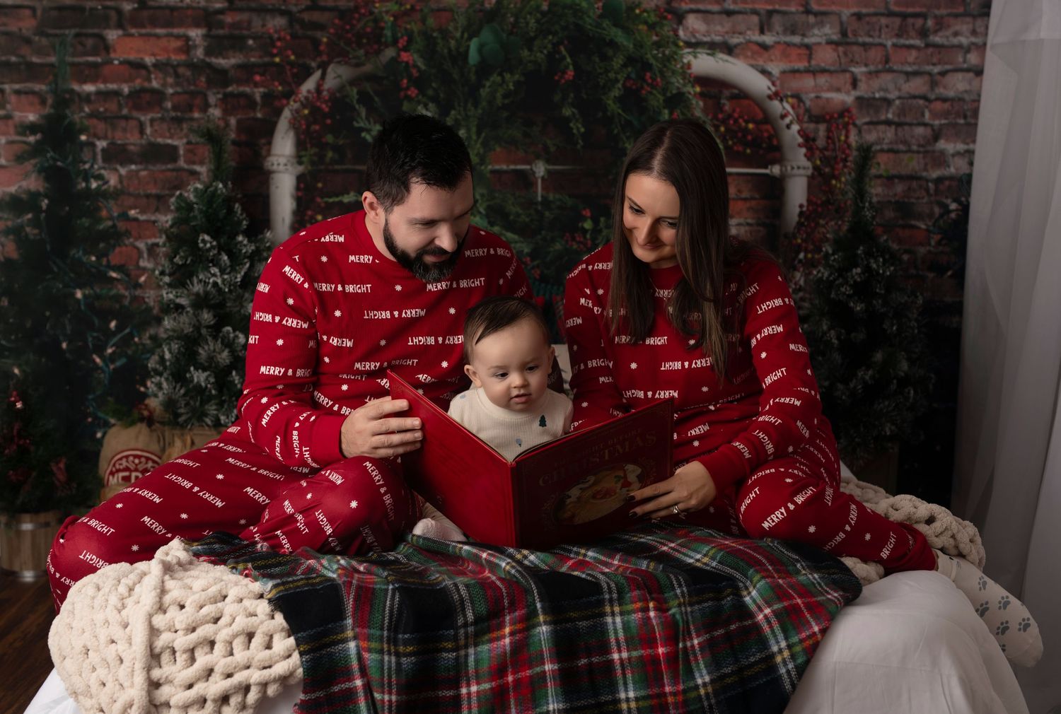 Family in matching red Christmas pajamas reading a book together with their newborn baby. christmas miini family photoshoot