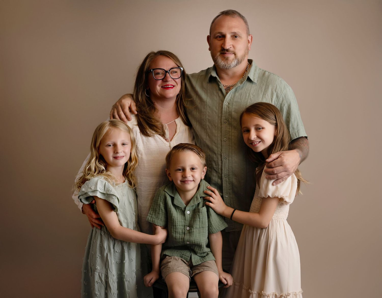 Family of five posing for a studio portrait, parents with three young children in coordinating earth-tone outfits.