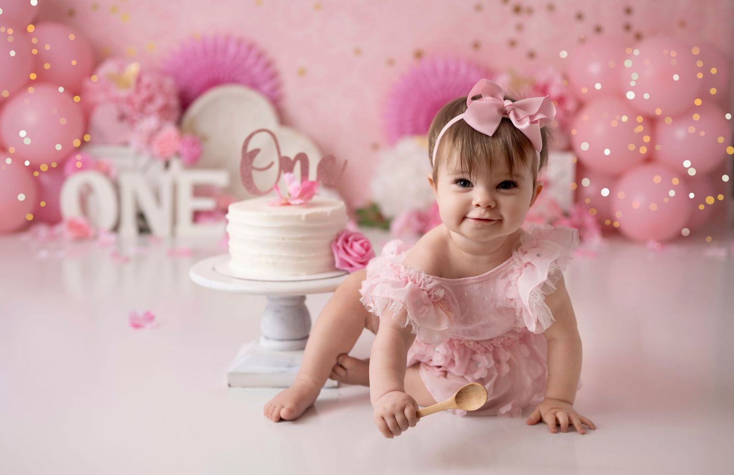 Happy baby girl in pink ruffle dress celebrating first birthday with cake and balloon decorations. pink theme