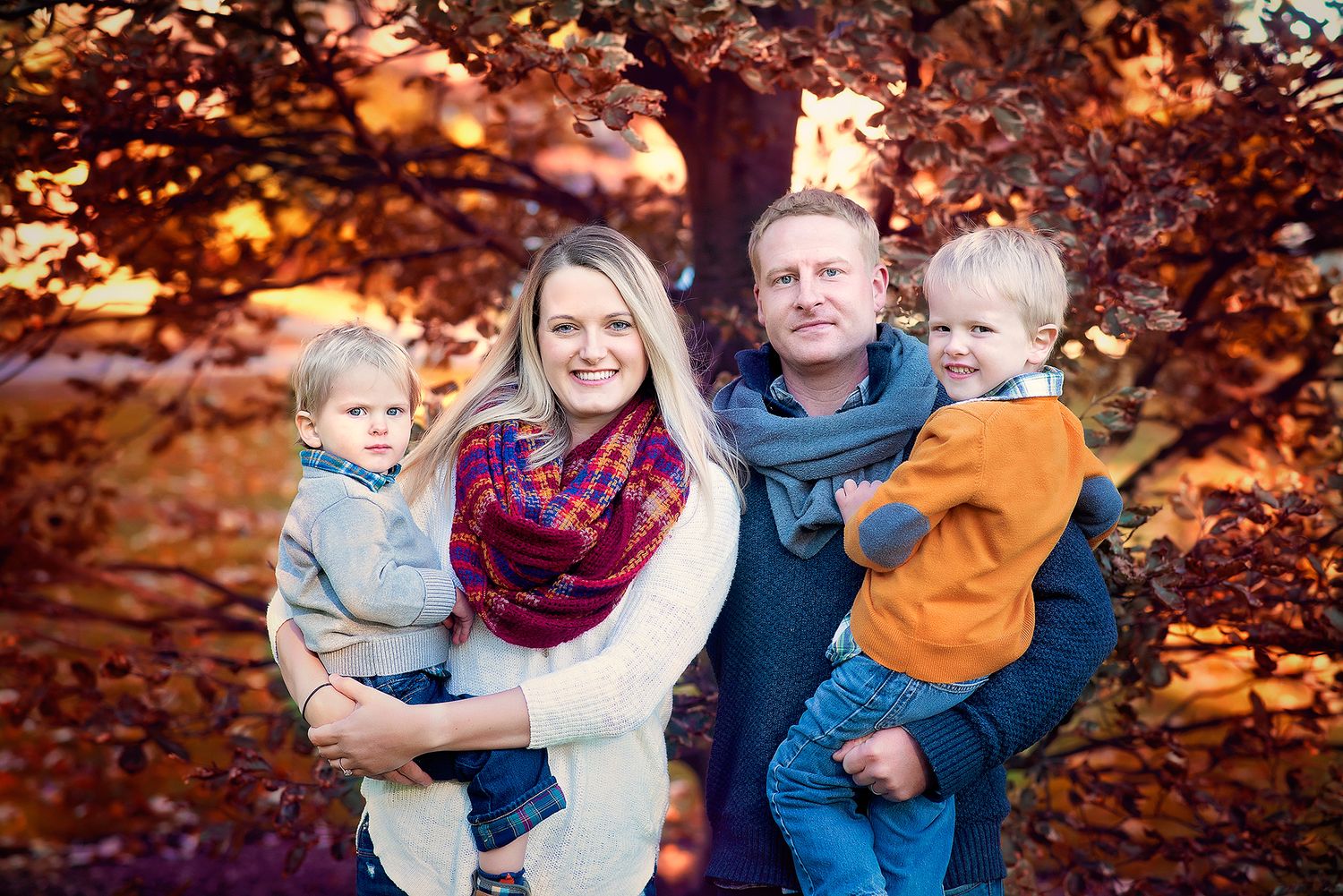 Happy family of four posing outdoors among vibrant autumn foliage at sunset.