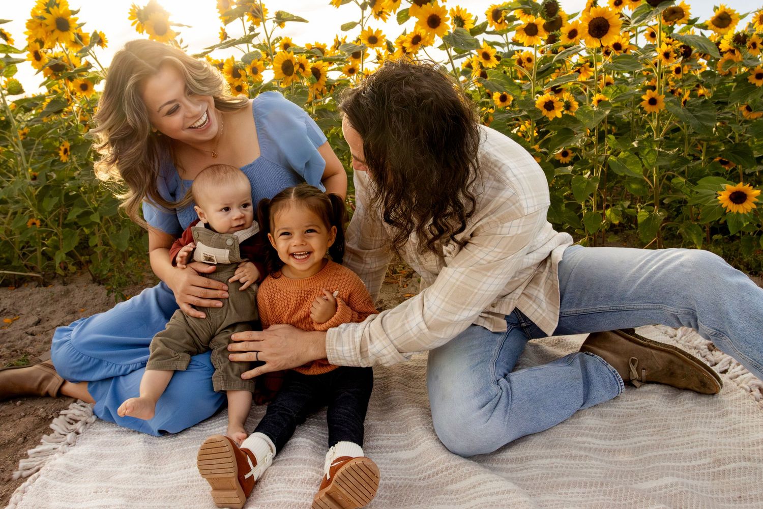 Family lying on blanket in autumn garden with golden flowers and sunlight creating warm, joyful atmosphere.