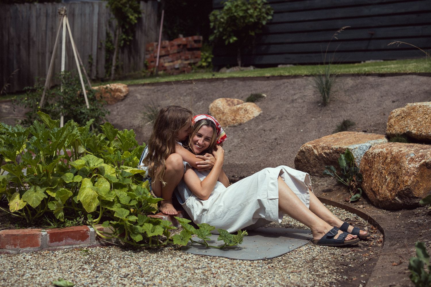 A couple relaxes together on a blanket in a garden with decorative rocks and plants.