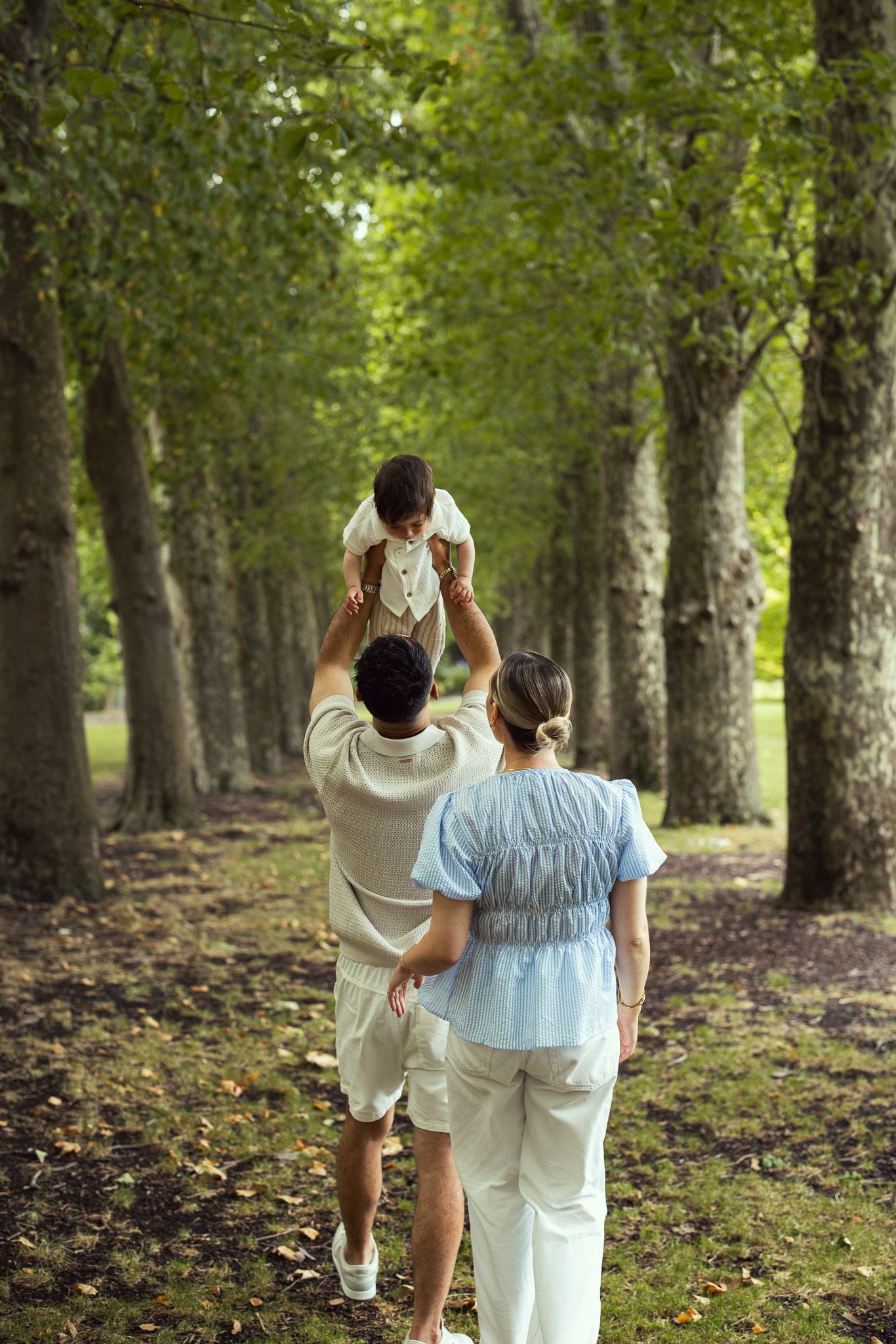 A group in white clothing walks together through a tree-lined path in a peaceful forest setting.