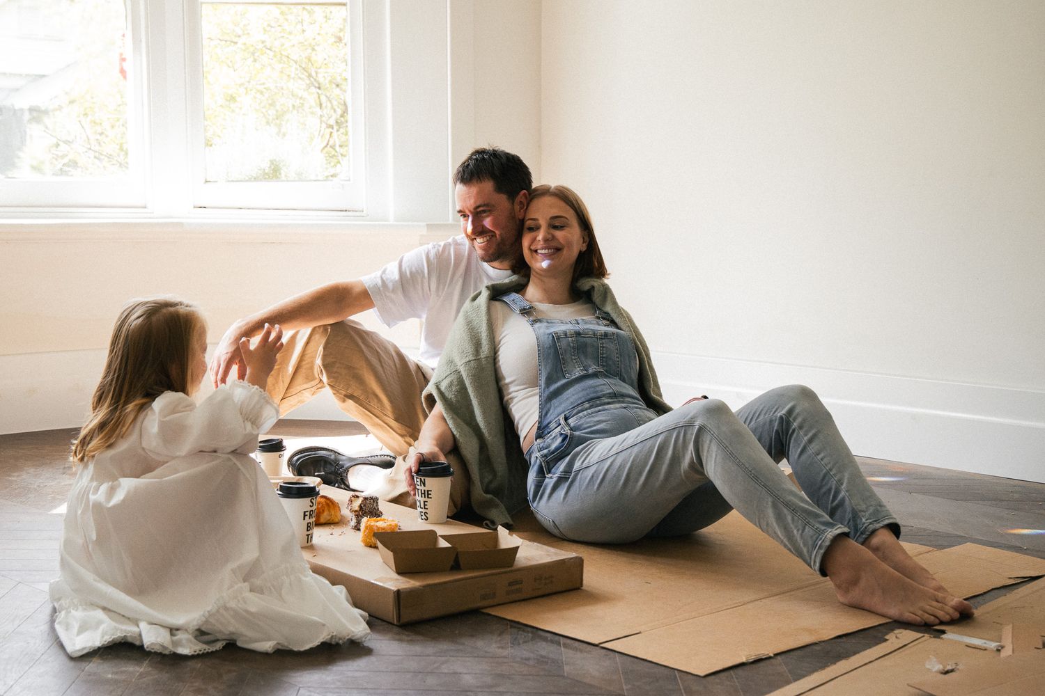 Happy family relaxing on floor during home renovation, parents smiling with young daughter playing nearby.