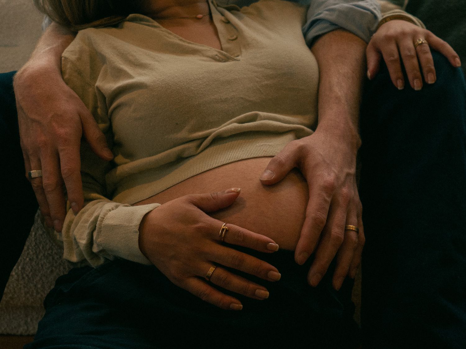 Close-up view of hands resting gently on a baby bump at a maternity family photoshoot.