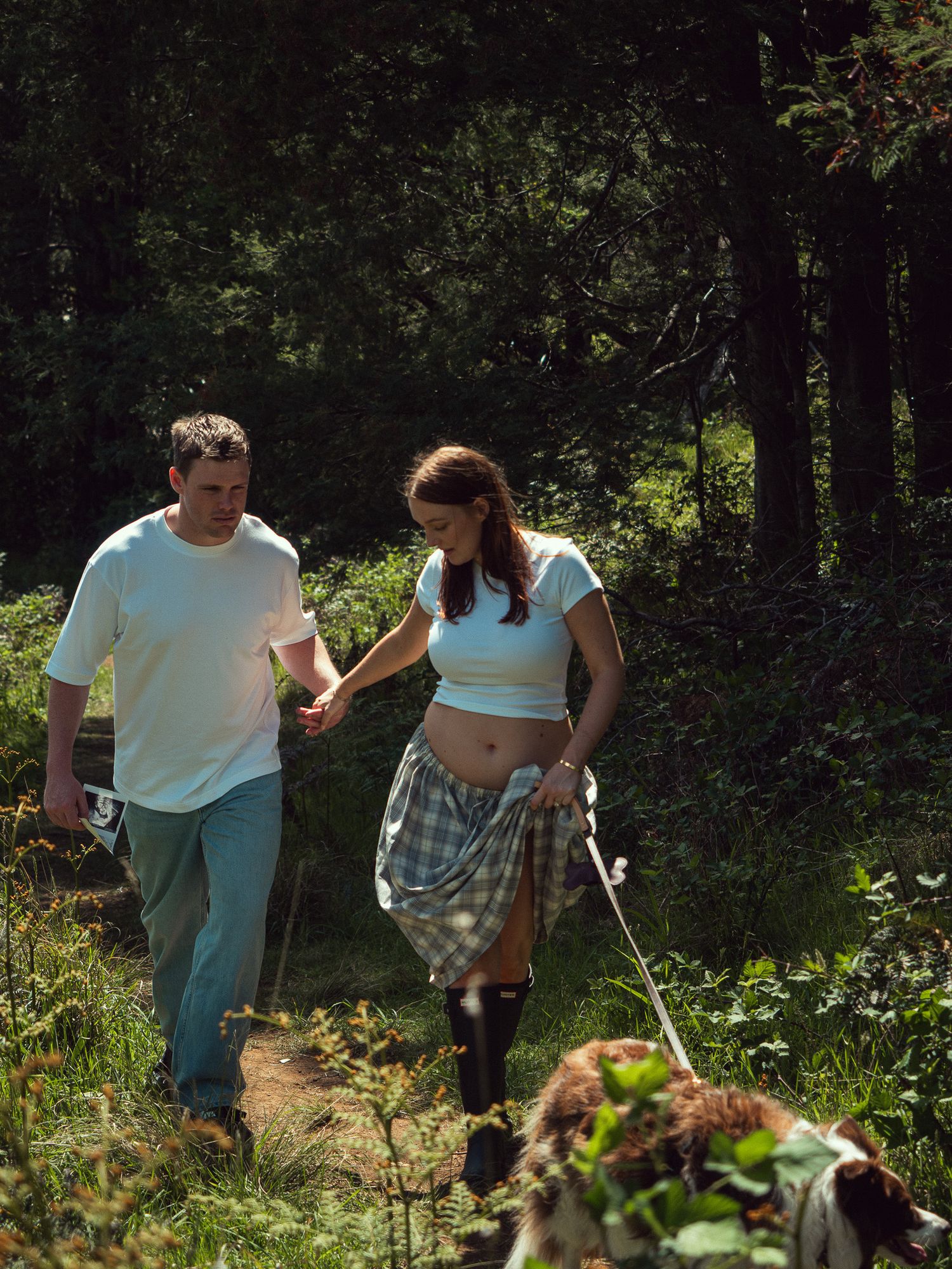 A group of people walk together on a dirt path through a wooded area on a sunny day.