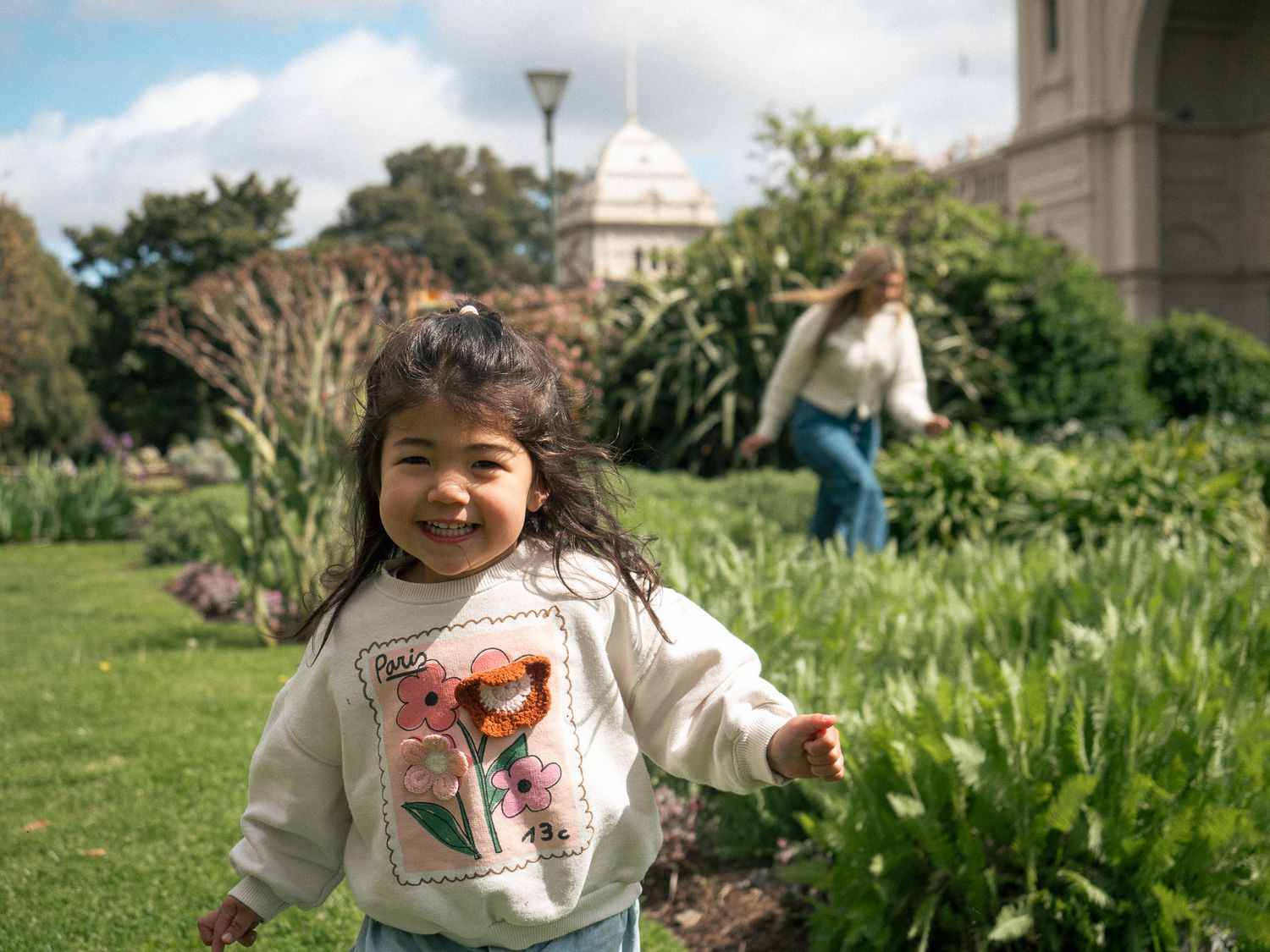 A young person plays joyfully in a lush green garden with blooming spring flowers and plants.