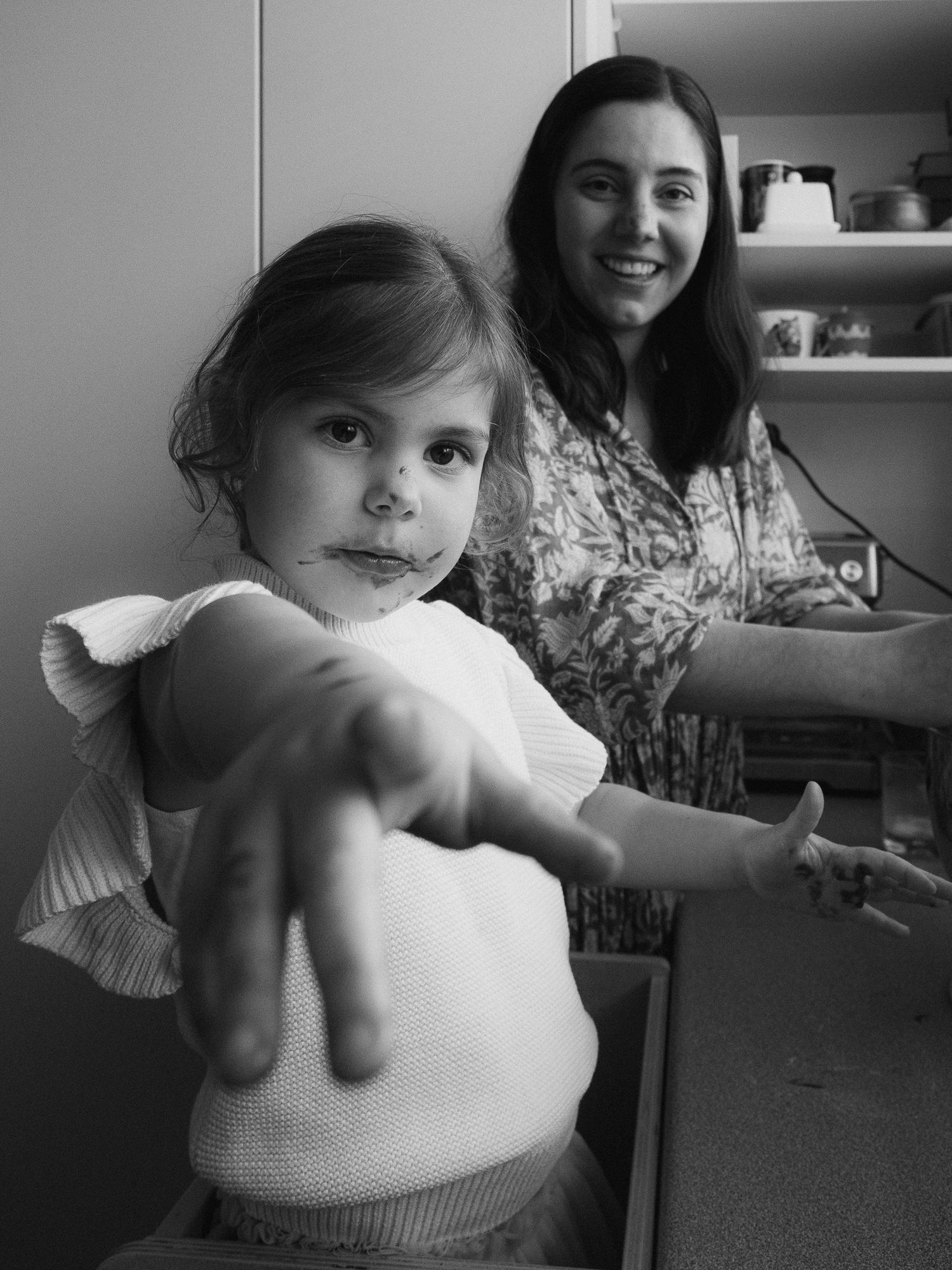 Black and white image of a motherhood session where they're baking, both looking at the camera and daughter pointing at the camera.