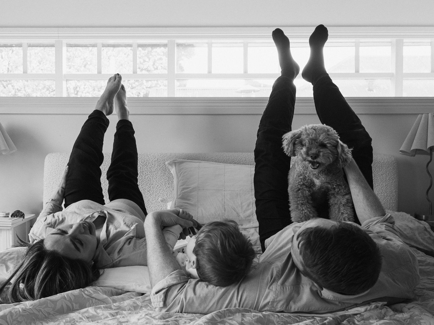 Black and white image of a family relaxing and lying down in a bright bedroom.