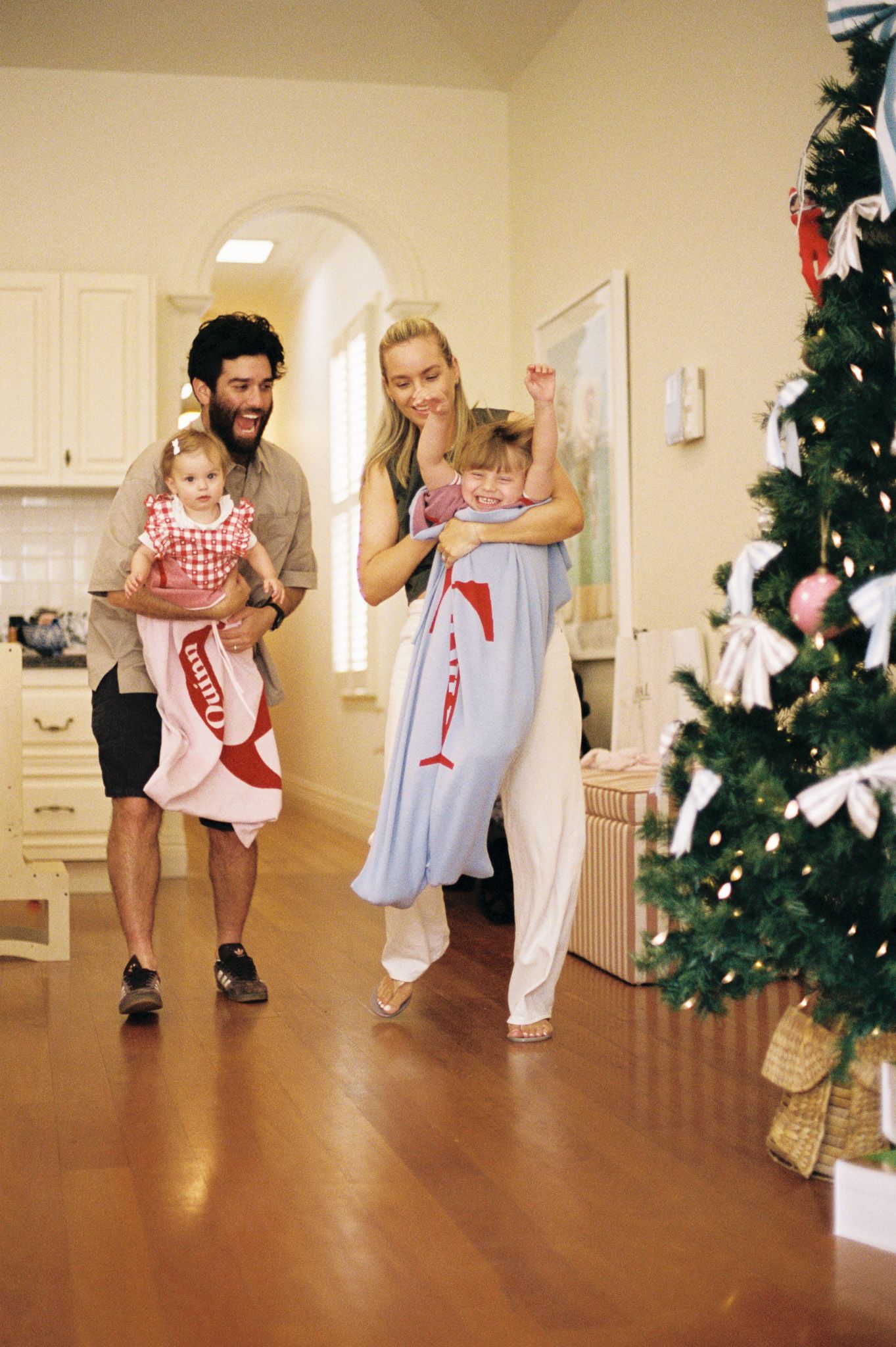 A family stands in their kitchen wearing matching red and white holiday outfits next to a decorated Christmas tree.