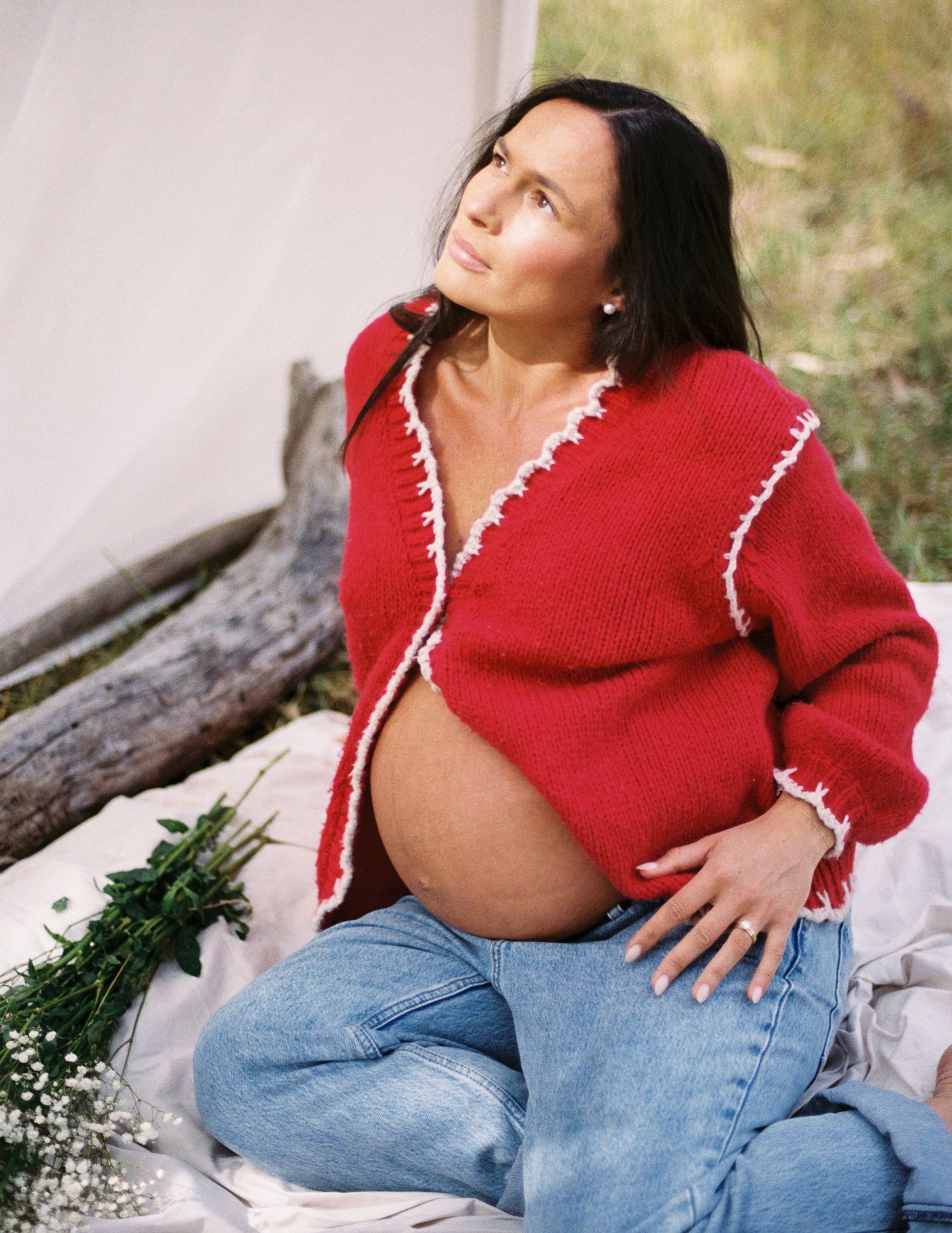 A person in a red sweater and jeans sits on a bench in a casual outdoor setting.