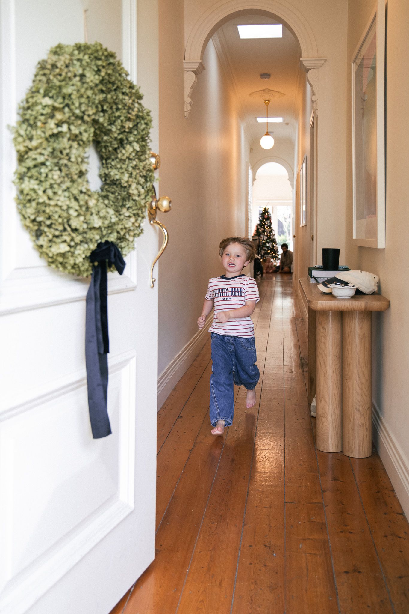 Three sequential photos show a long hallway with hardwood floors, white walls, and decorative greenery on display.