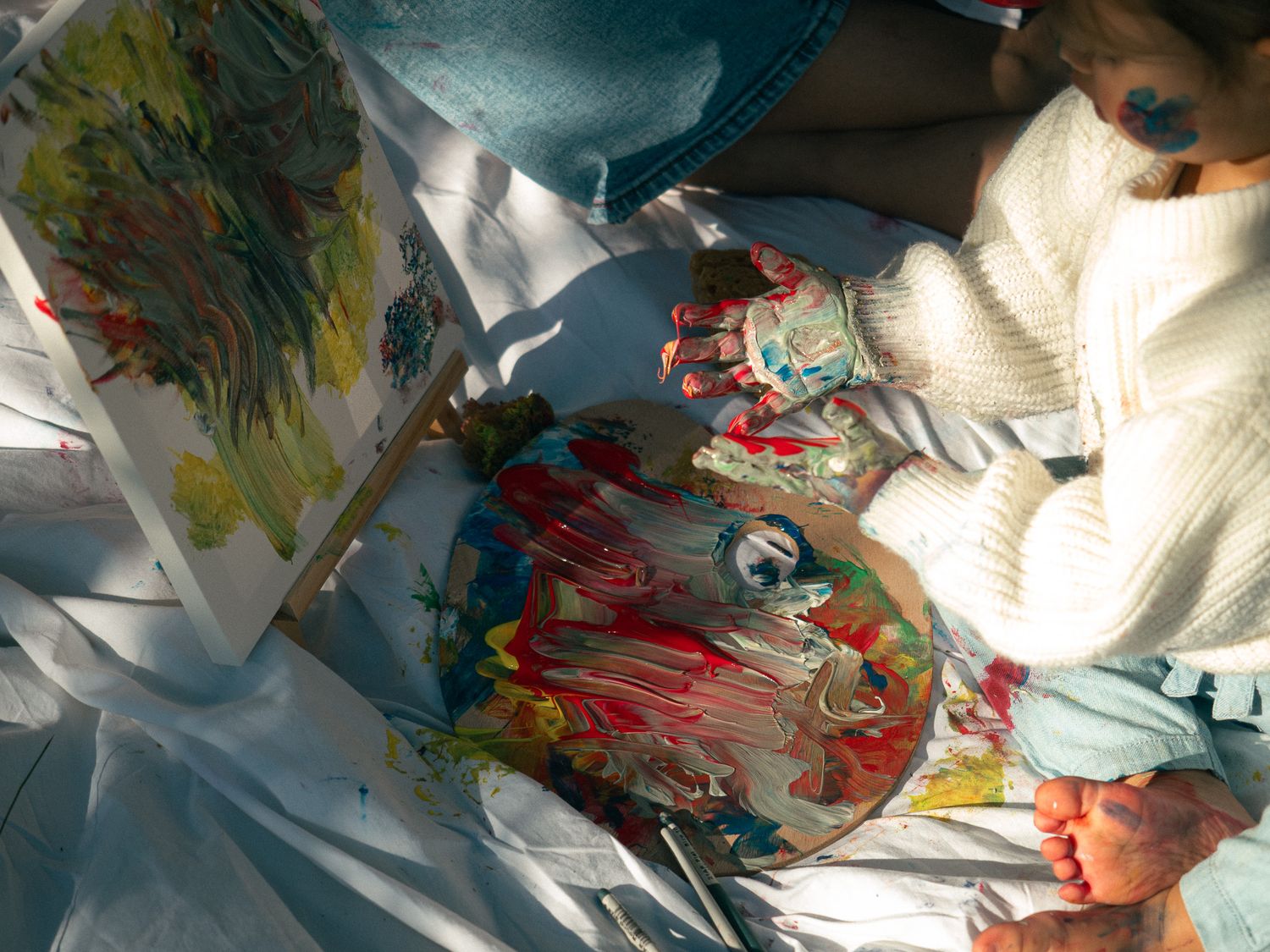 A close-up photo of a toddler's hands covered in paint as she gets creative with her mum during a motherhood photoshoot in a park.