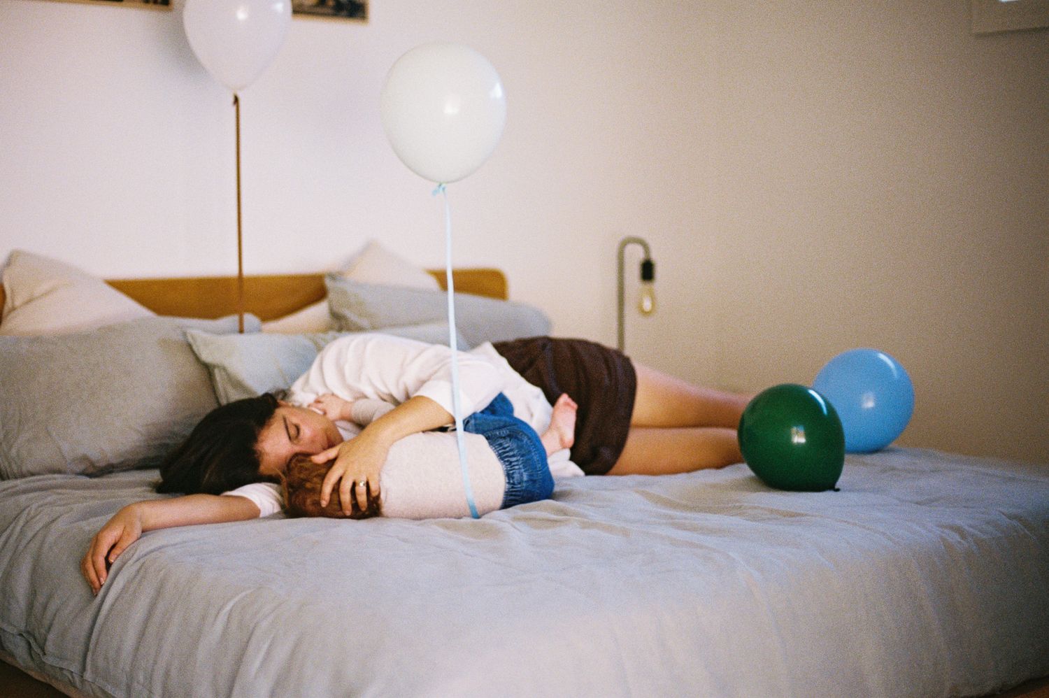 Person lying on a bed surrounded by white, blue, and green balloons in a cozy bedroom setting.
