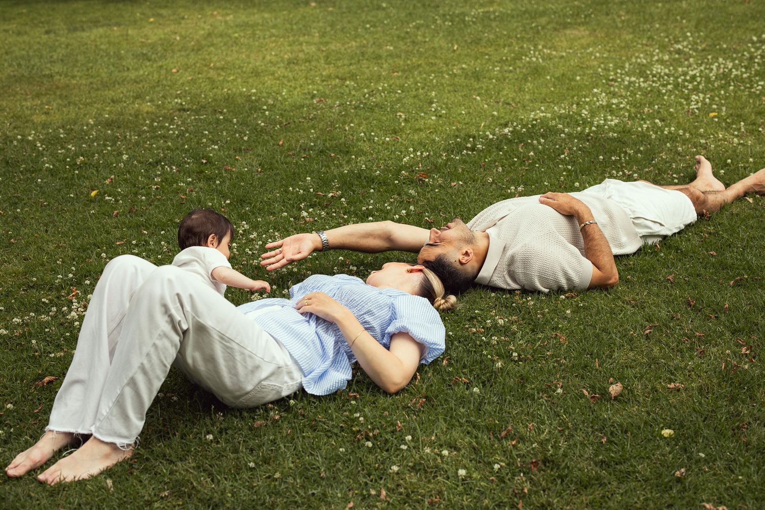 Three people lying on grass in casual summer clothing relaxing outdoors on a sunny day.