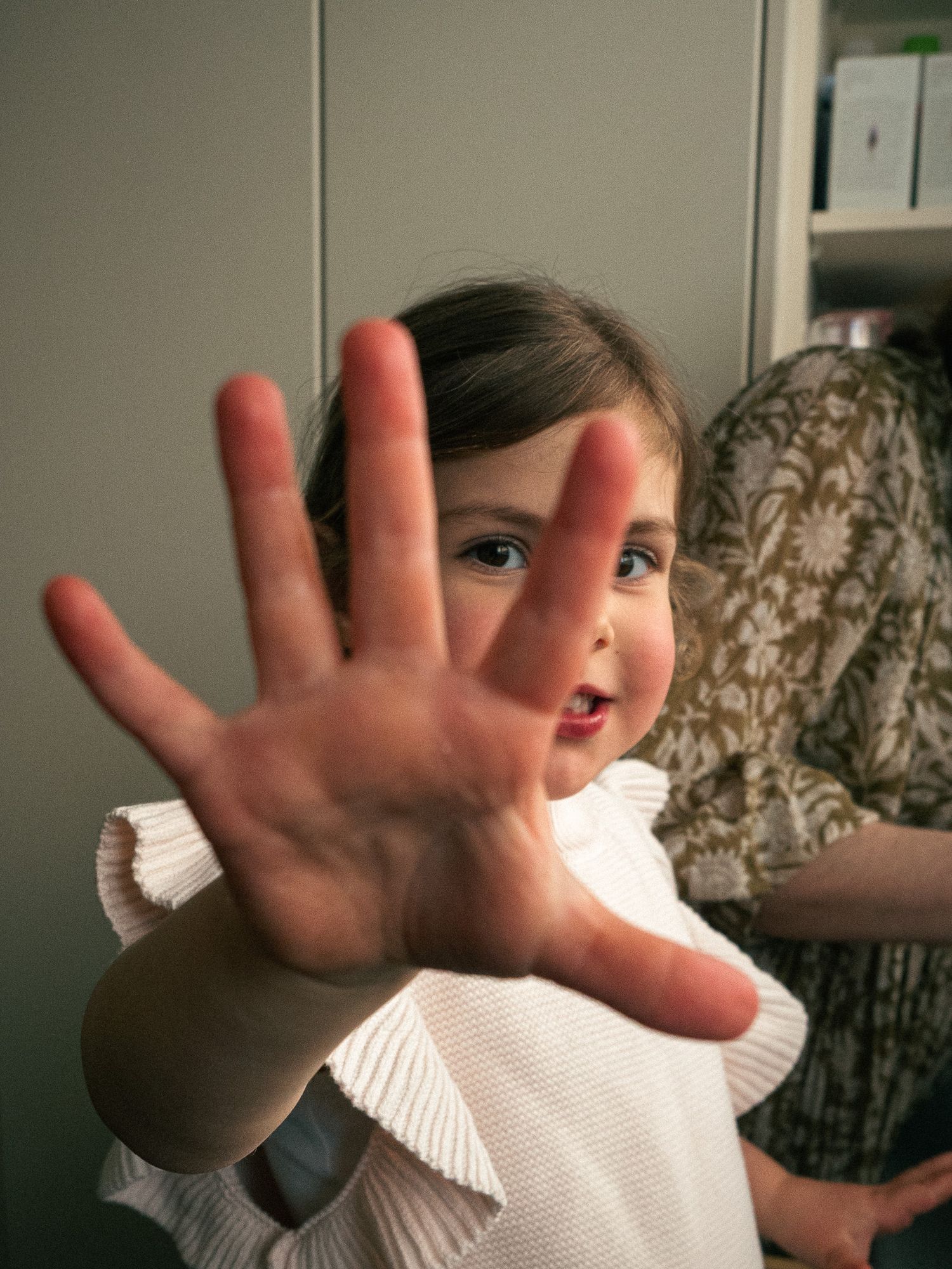 Child in white sweater reaching towards camera with outstretched hands in a kitchen in Melbourne.