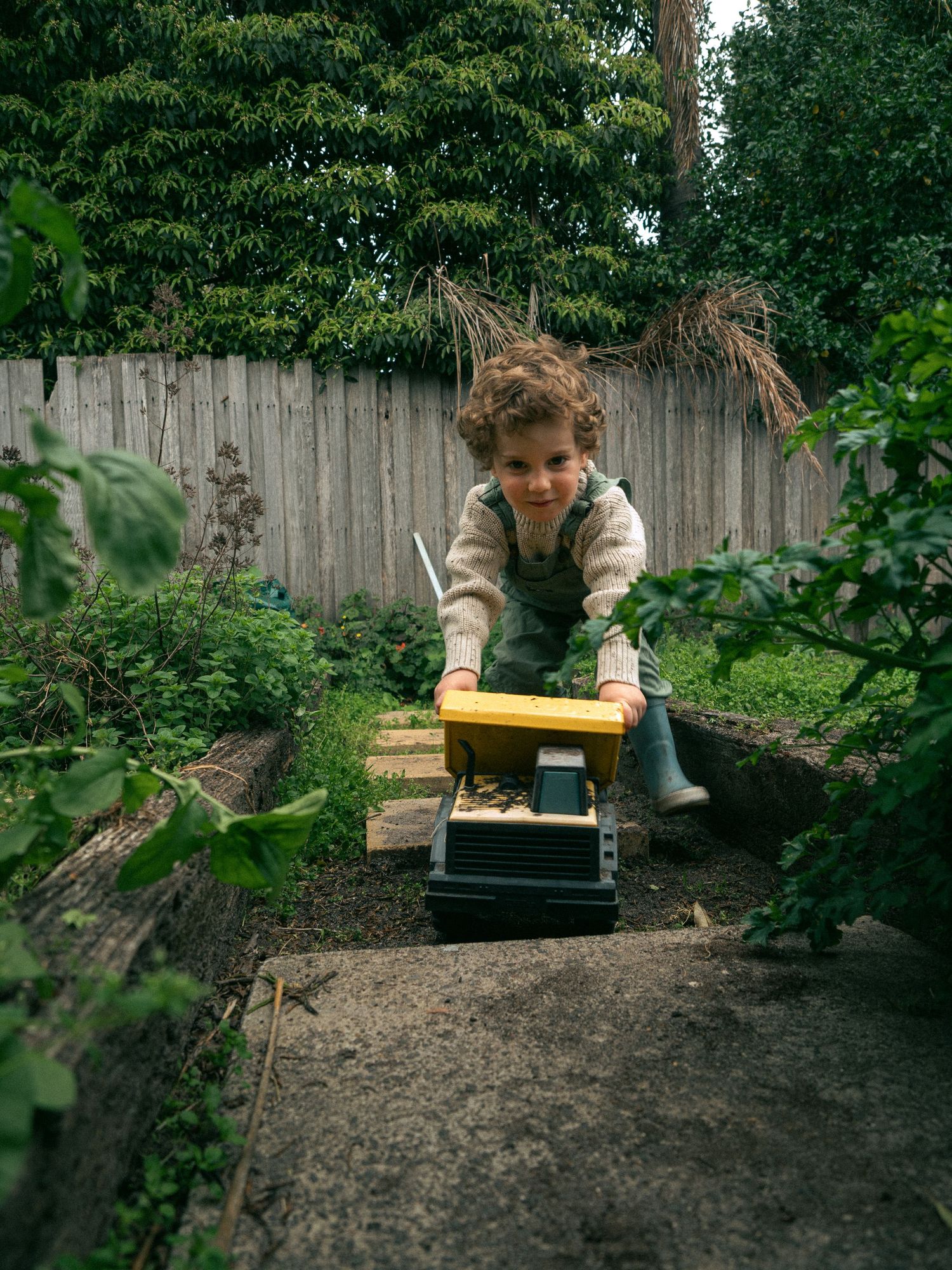 A garden scene of a young boy playing in gumboots during his family photoshoot.